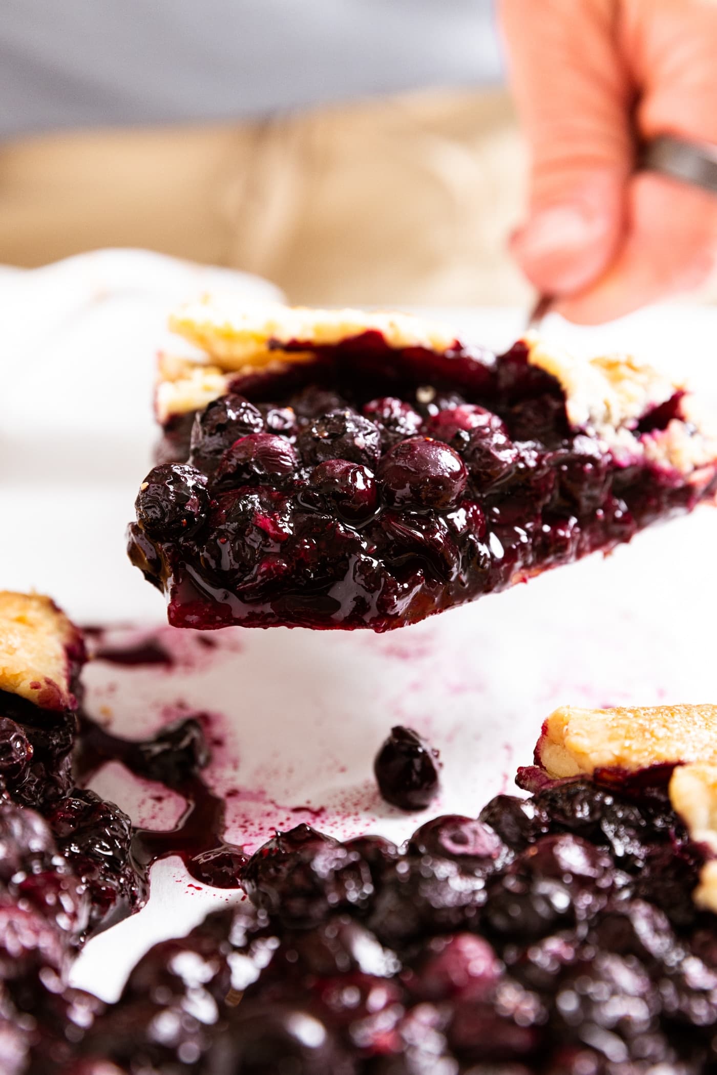 Hand holding pie serve with piece of blueberry galette with rest of galette below.