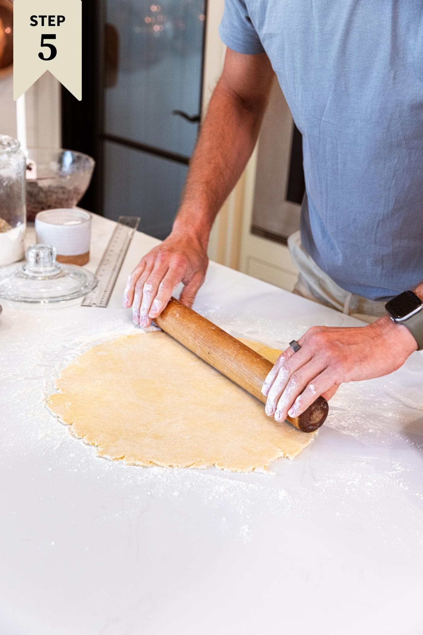 Two hands using rolling pin to roll out pie crust on white countertop.
