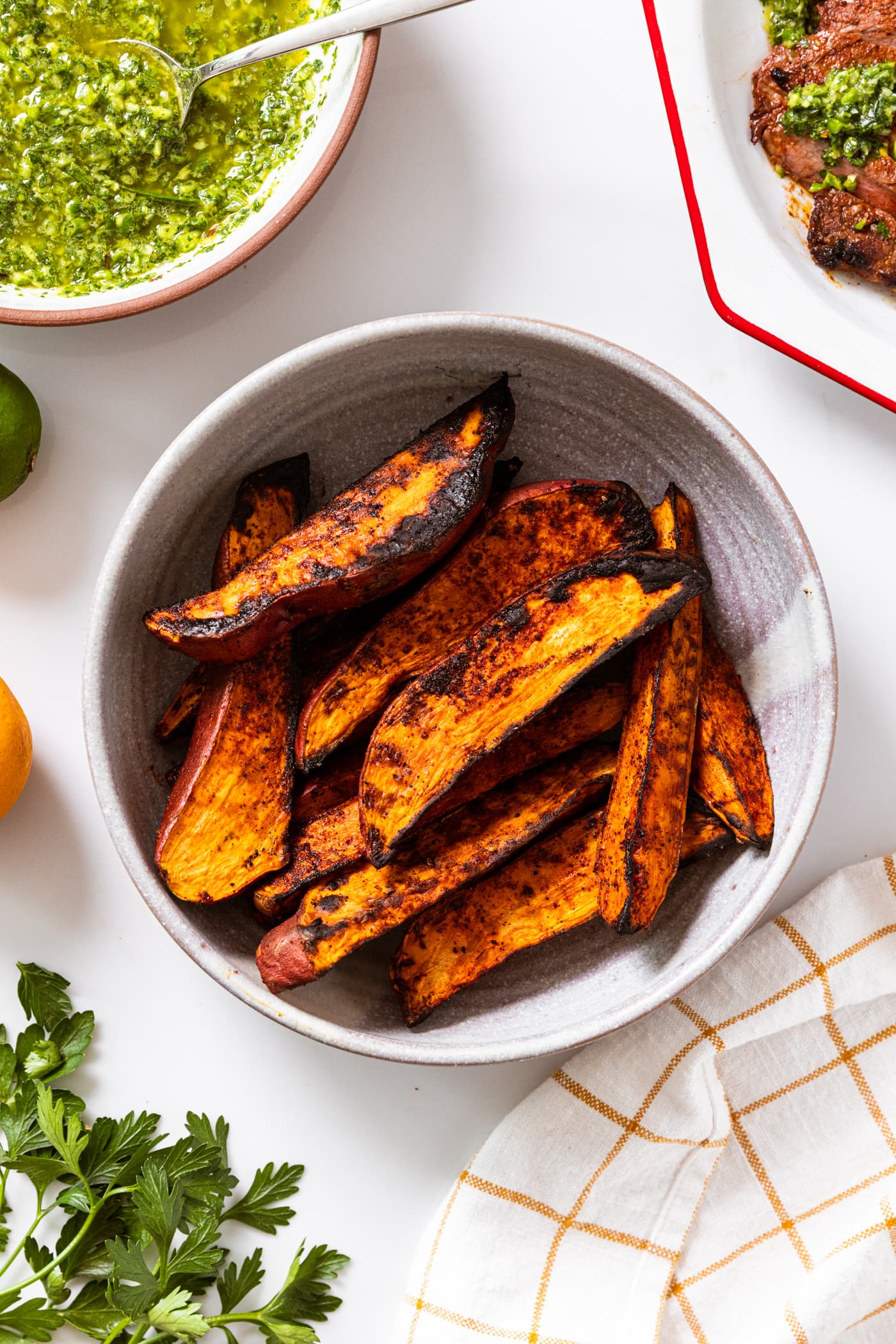 White countertop with stoneware bowl filled with sweet potato wedges with garlic scape chimichurri.