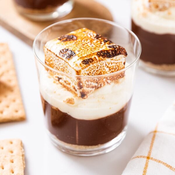 Glass filled with chocolate pudding, whipped cream, and a marshmallow on top with more cups in background also filled with pudding.