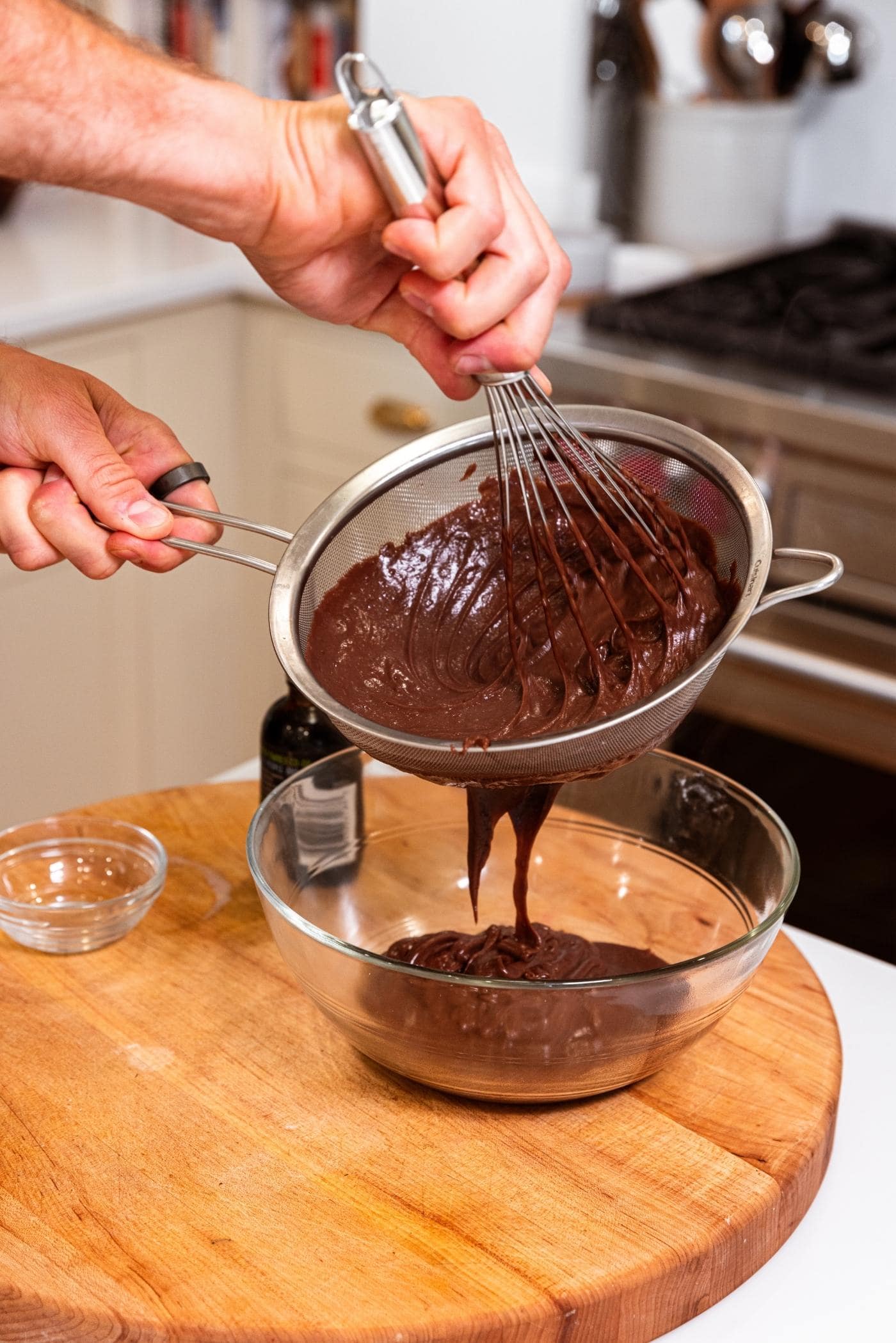 Hand stirring whisk in strainer to get chocolate mixture into glass bowl below.
