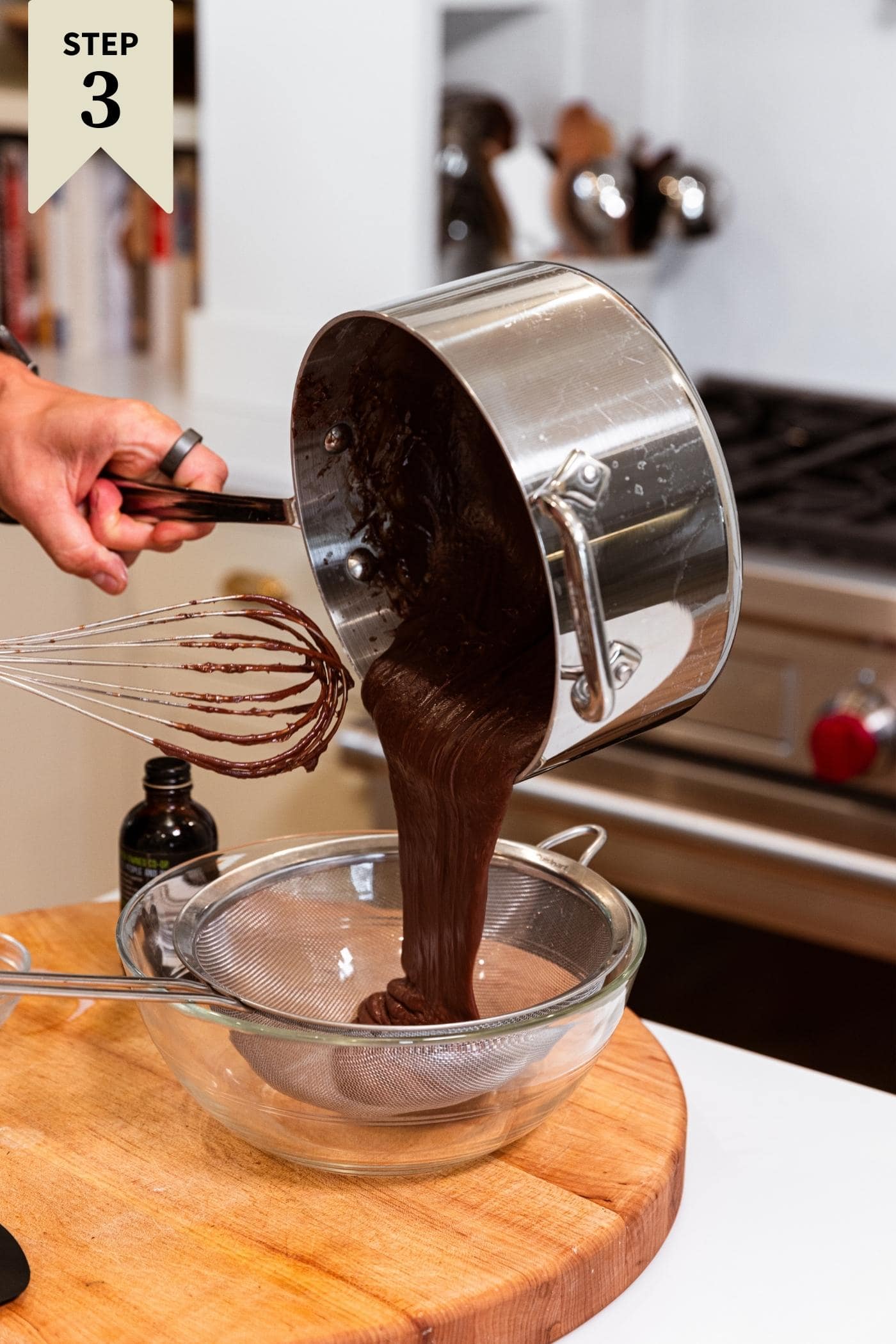 Hand pouring chocolate mixture from saucepan into strainer sitting in glass bowl.