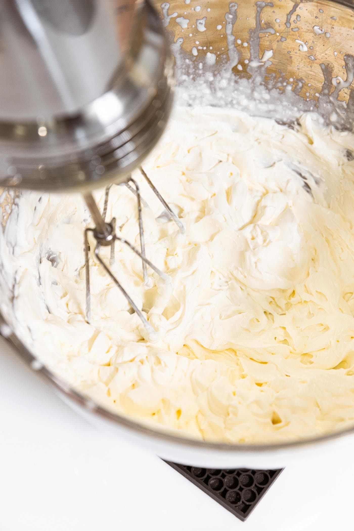 Whipped cream sitting in metal bowl after being whipped with hand mixer still in mixture.
