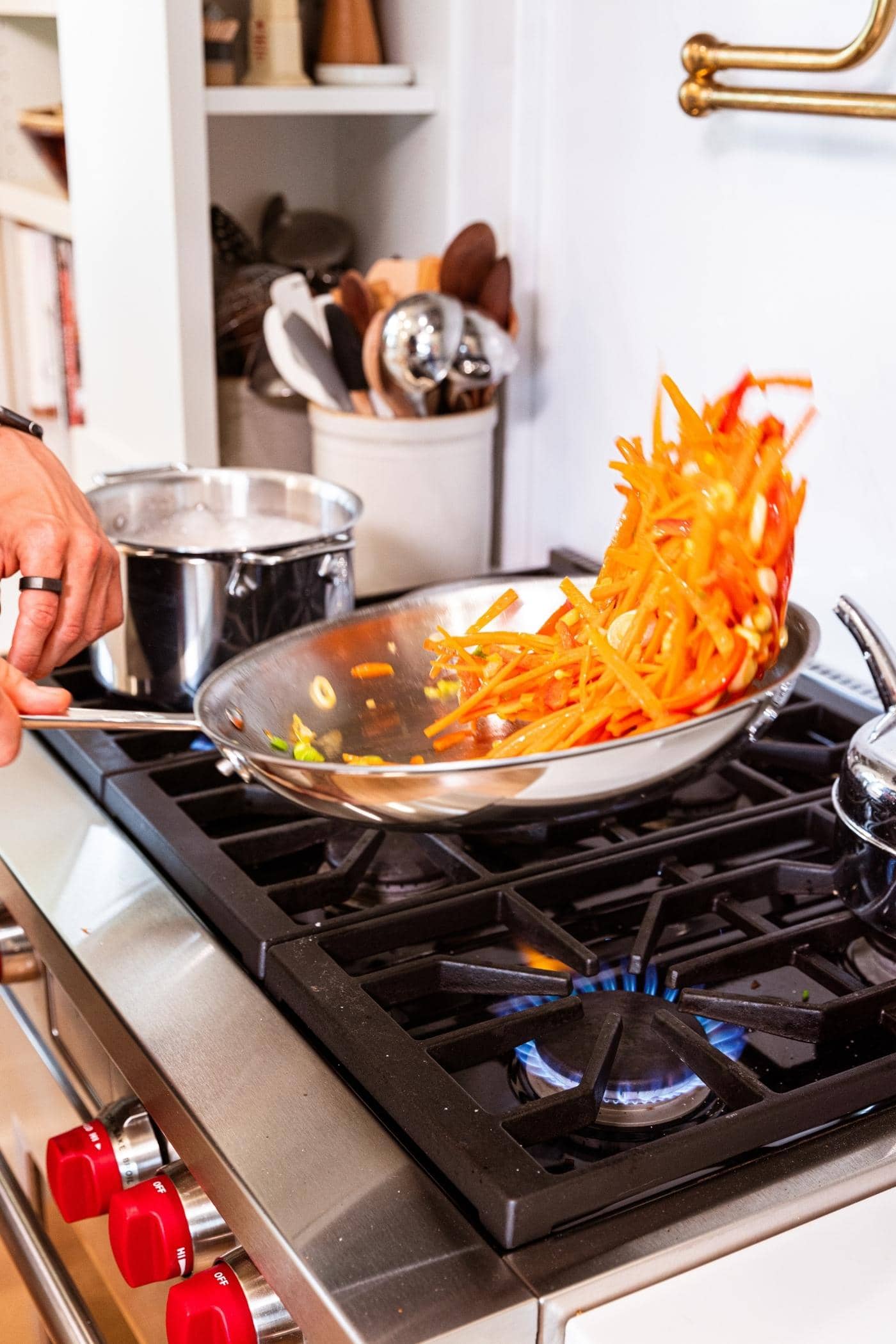 Hand holding skillet over stovetop sautéing contents with some almost flipping out of skillet.