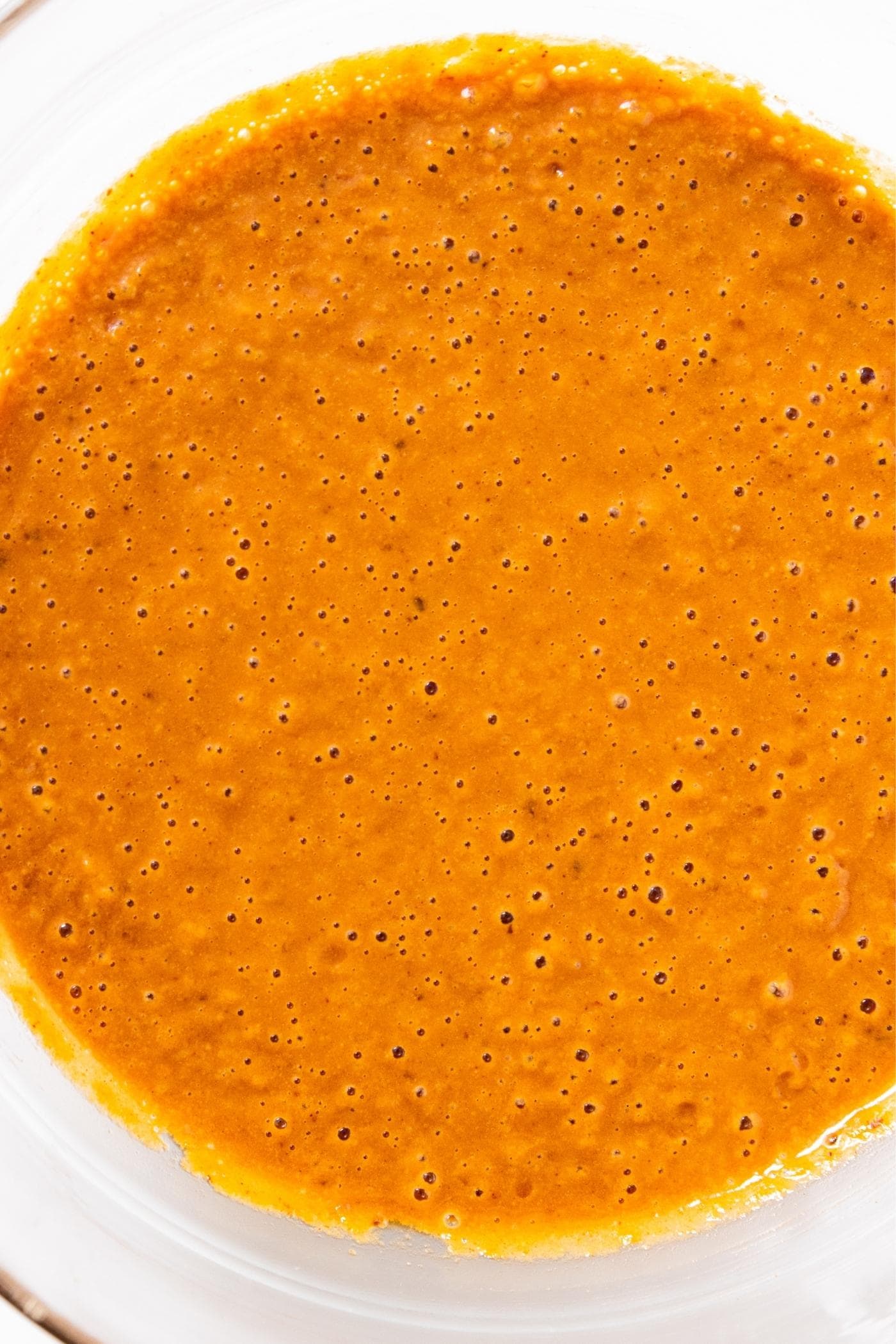 Glass bowl filled with peanut sauce with an orange color.