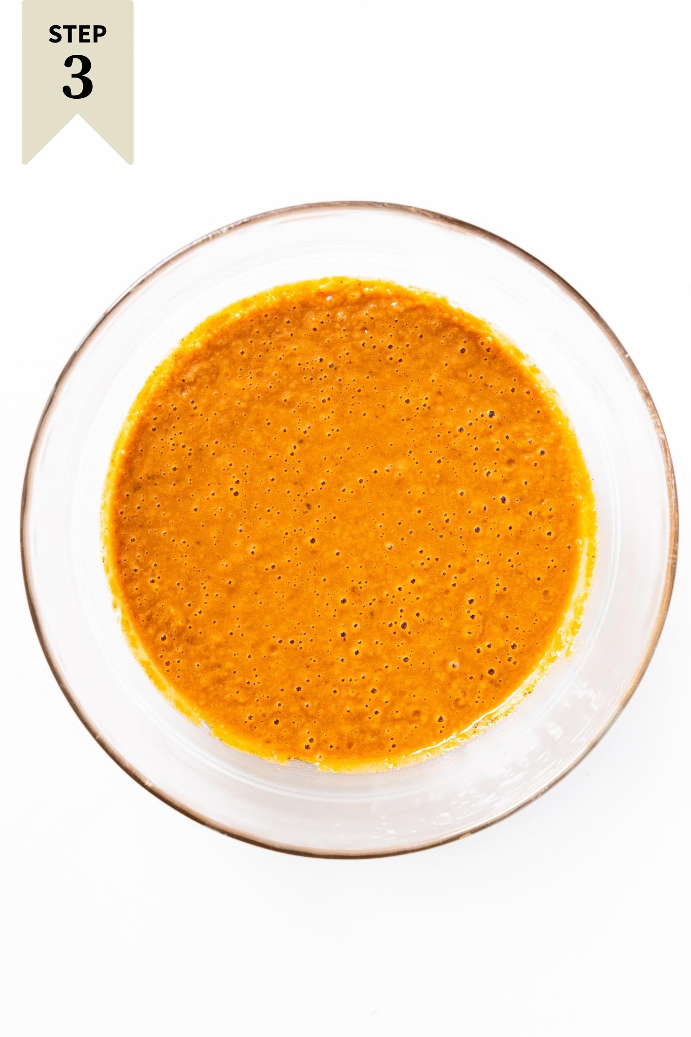 Glass bowl filled with orange colored peanut sauce sitting on white countertop.