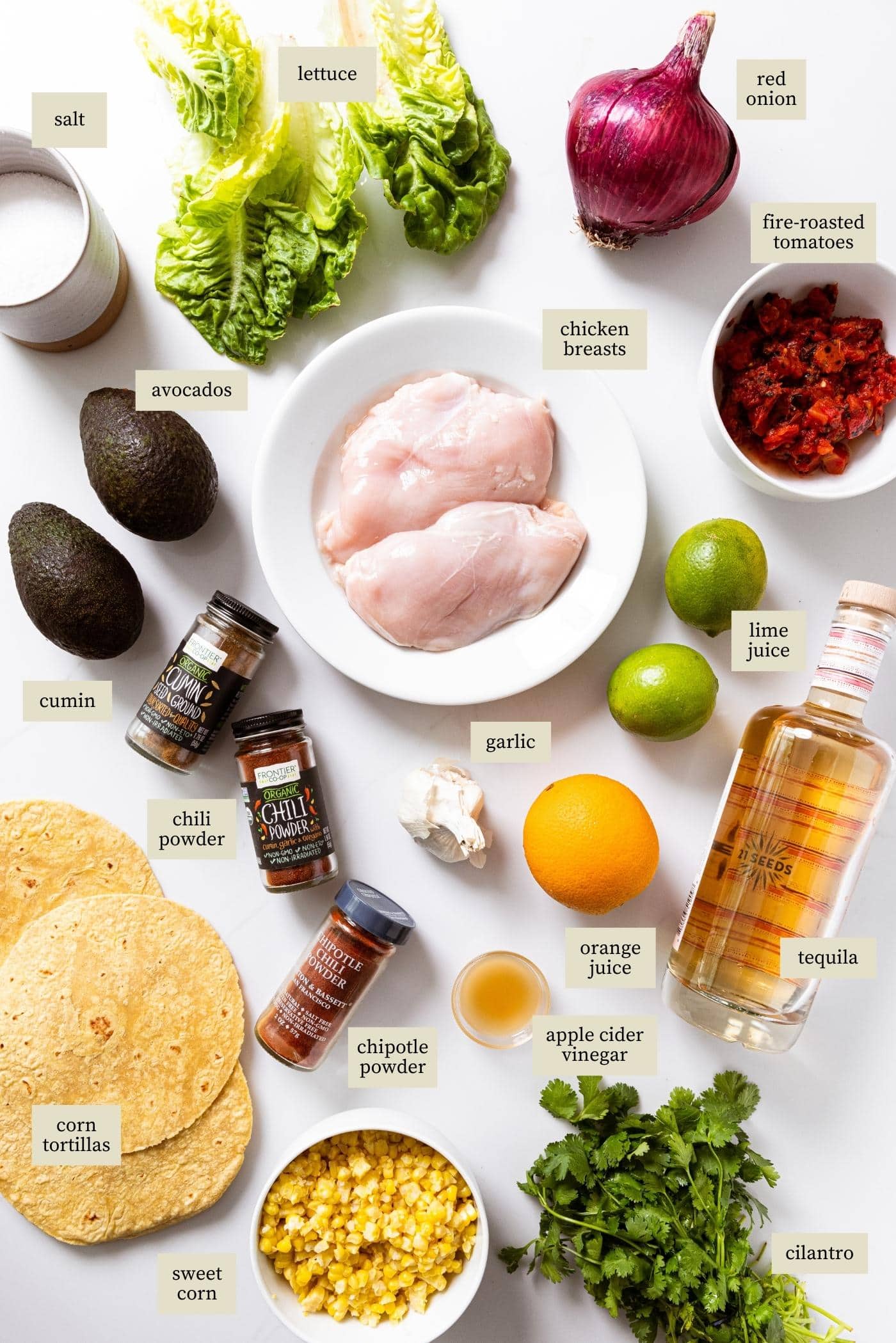 Lots of ingredients sitting on white countertop with labels indicating each item on counter which includes chicken, citrus, tequila, tortillas, tomatoes, and more.