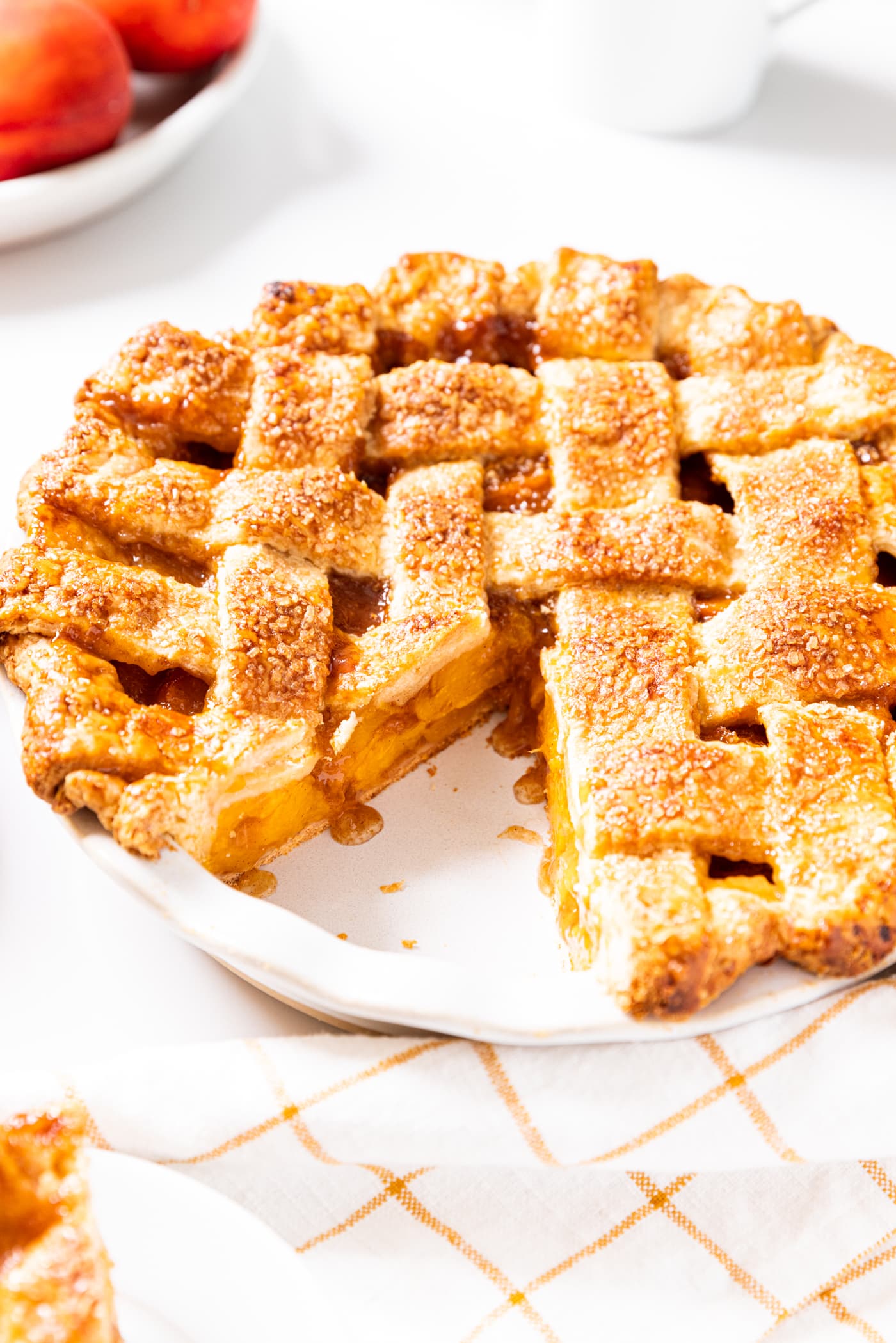 Peach pie with slice taken out sitting on white countertop with bowl filled with peaches in background.