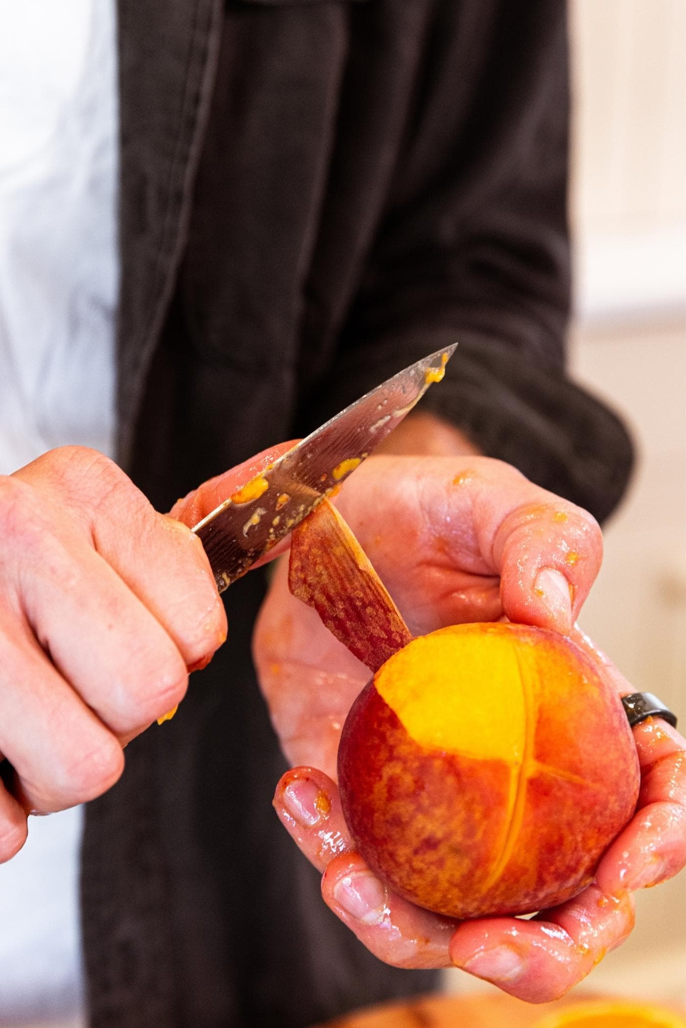 Hand holding knife peeling the skin off of a peach.