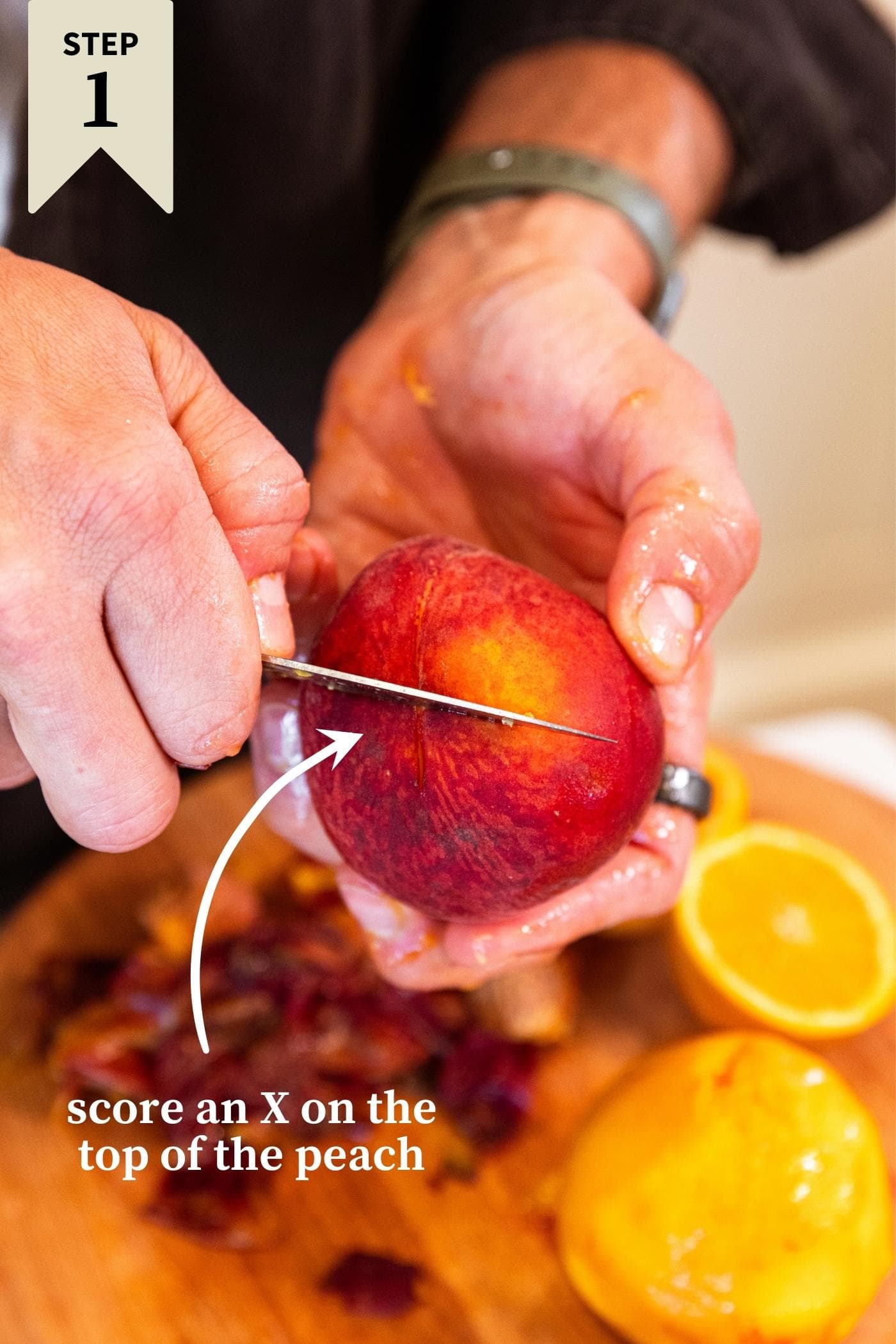 Hand holding unpeeled peach with knife cutting an X into the top of peach with with peach below.