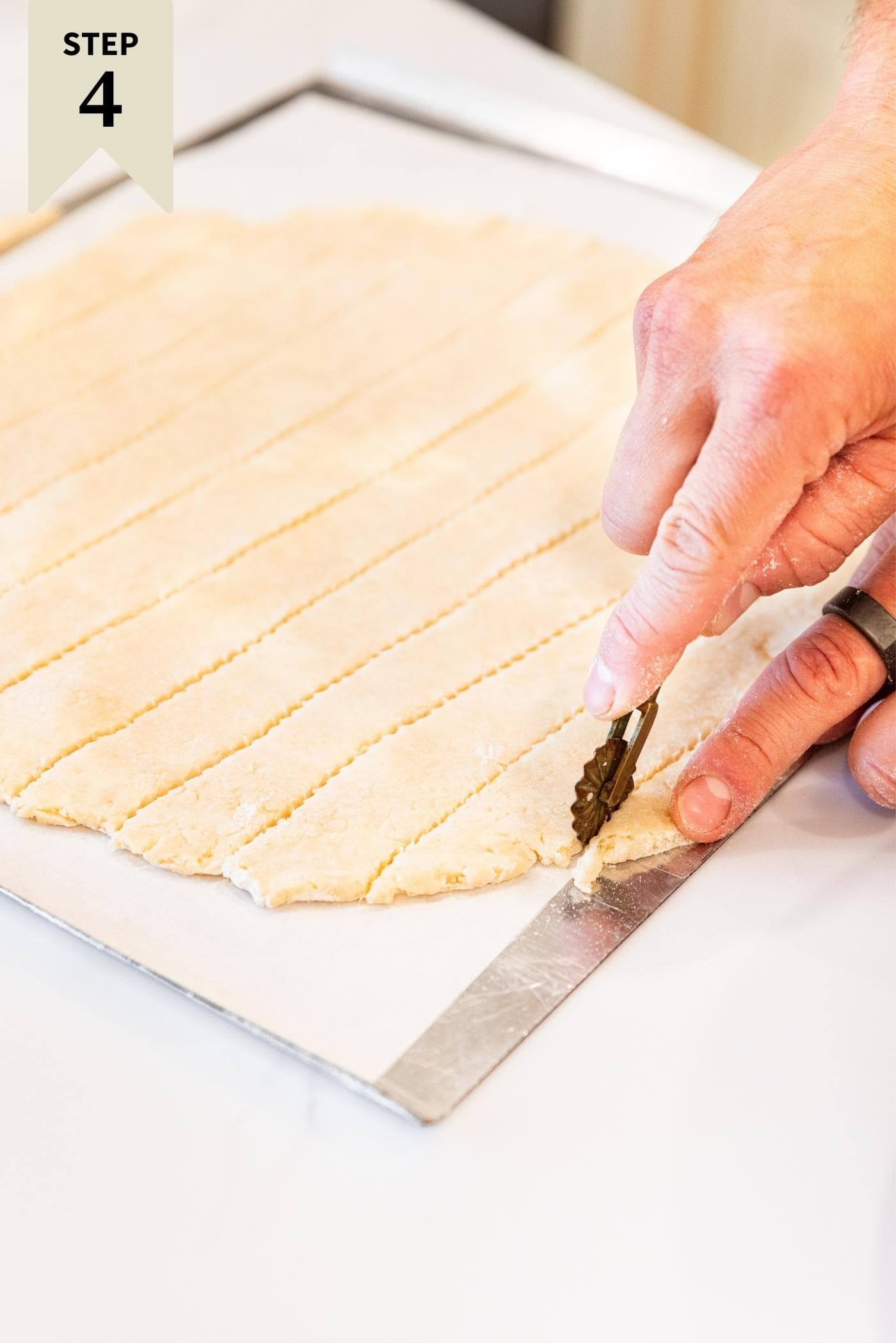 Hand cutting strips of pie crust from round circle all on white countertop.