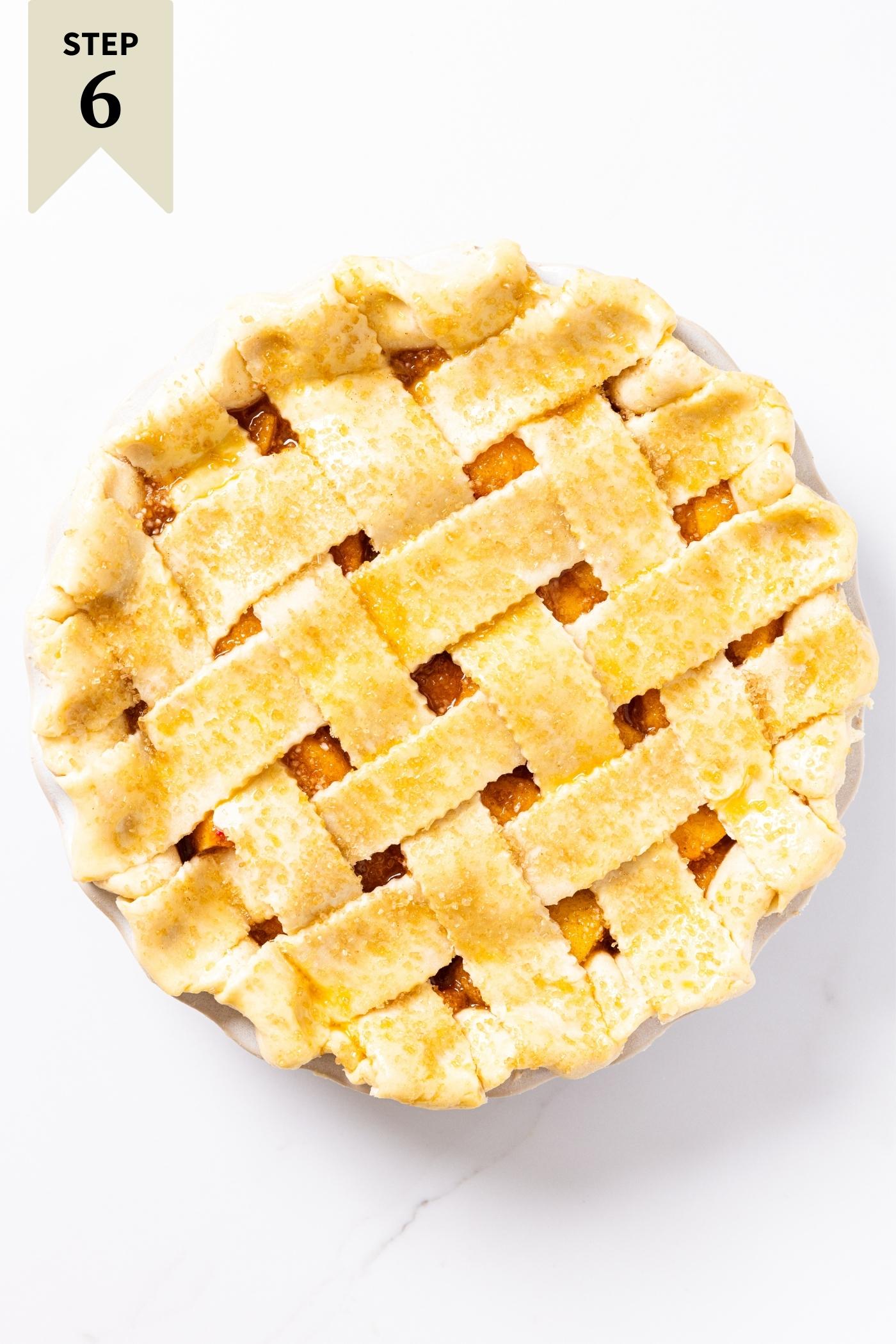 Unbaked pie with lattice top brushed with egg wash and turbinado sugar sitting on white countertop.