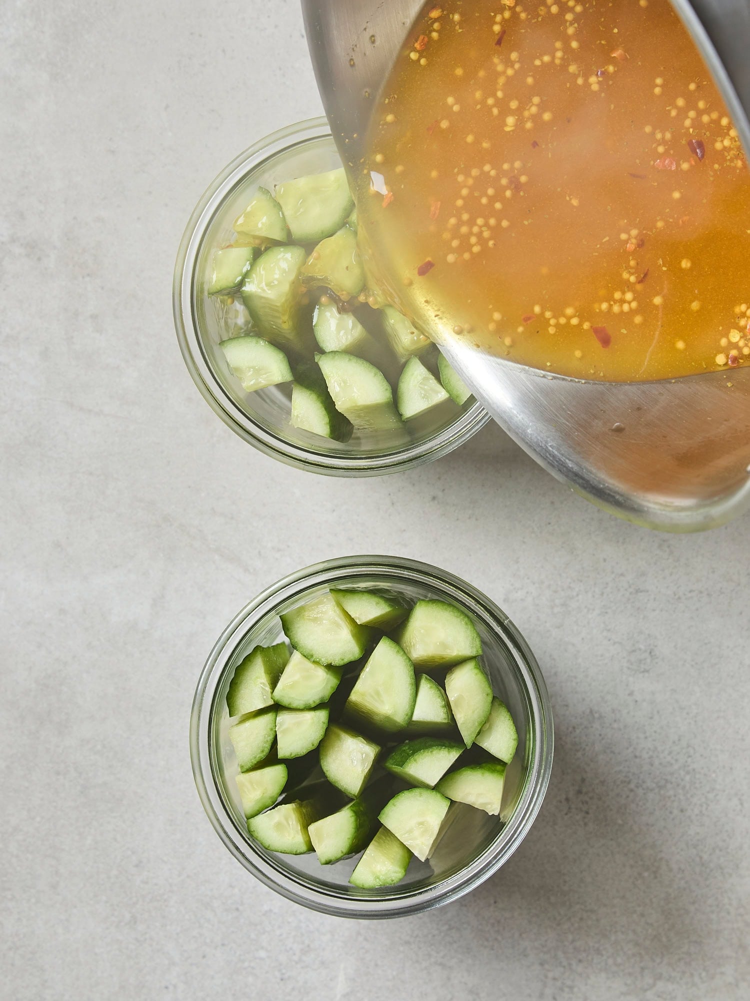Hot brine being poured over speared cucumbers to be made into pickles.