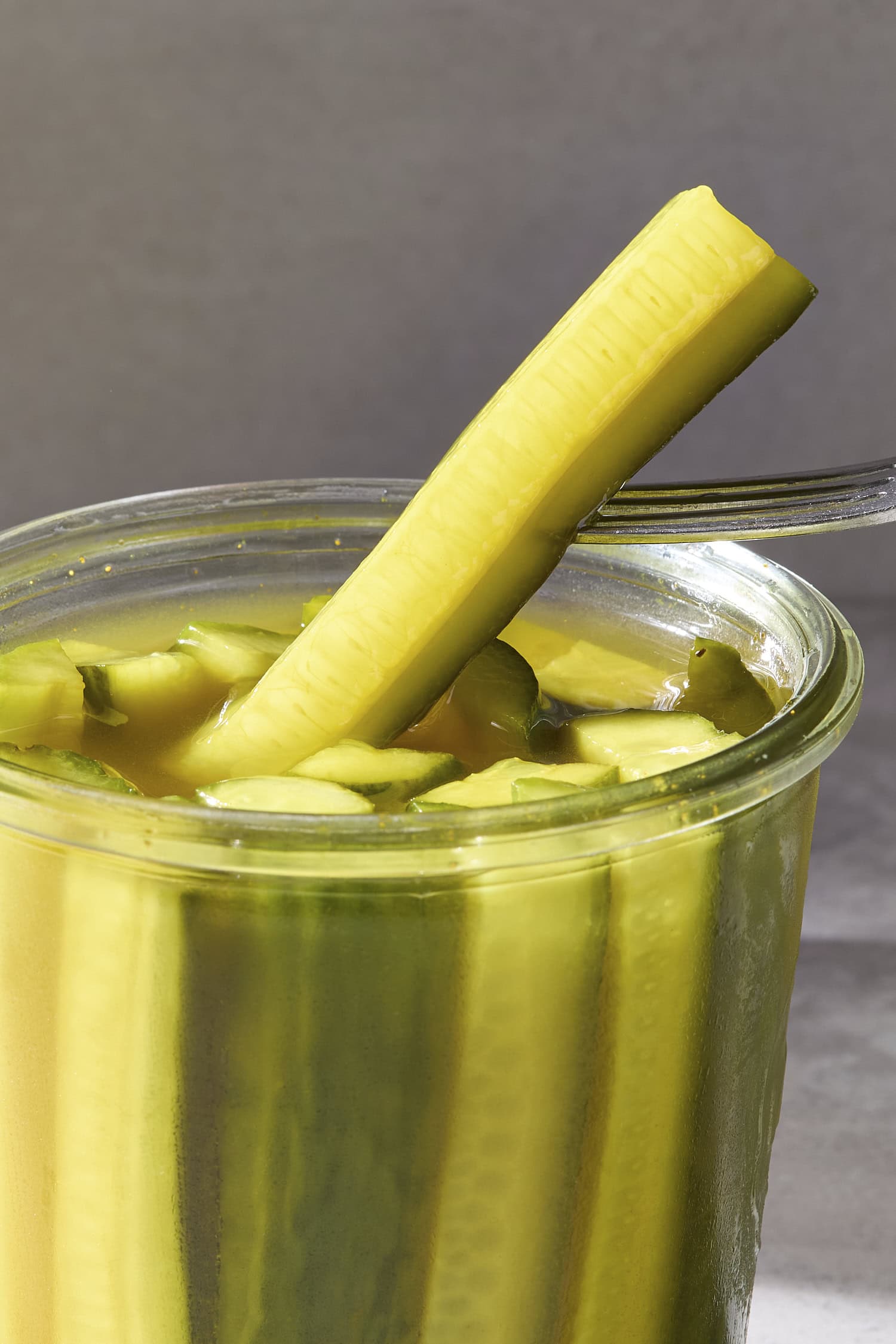 A fork pulling a speared pickle out of a brine-filled jar.