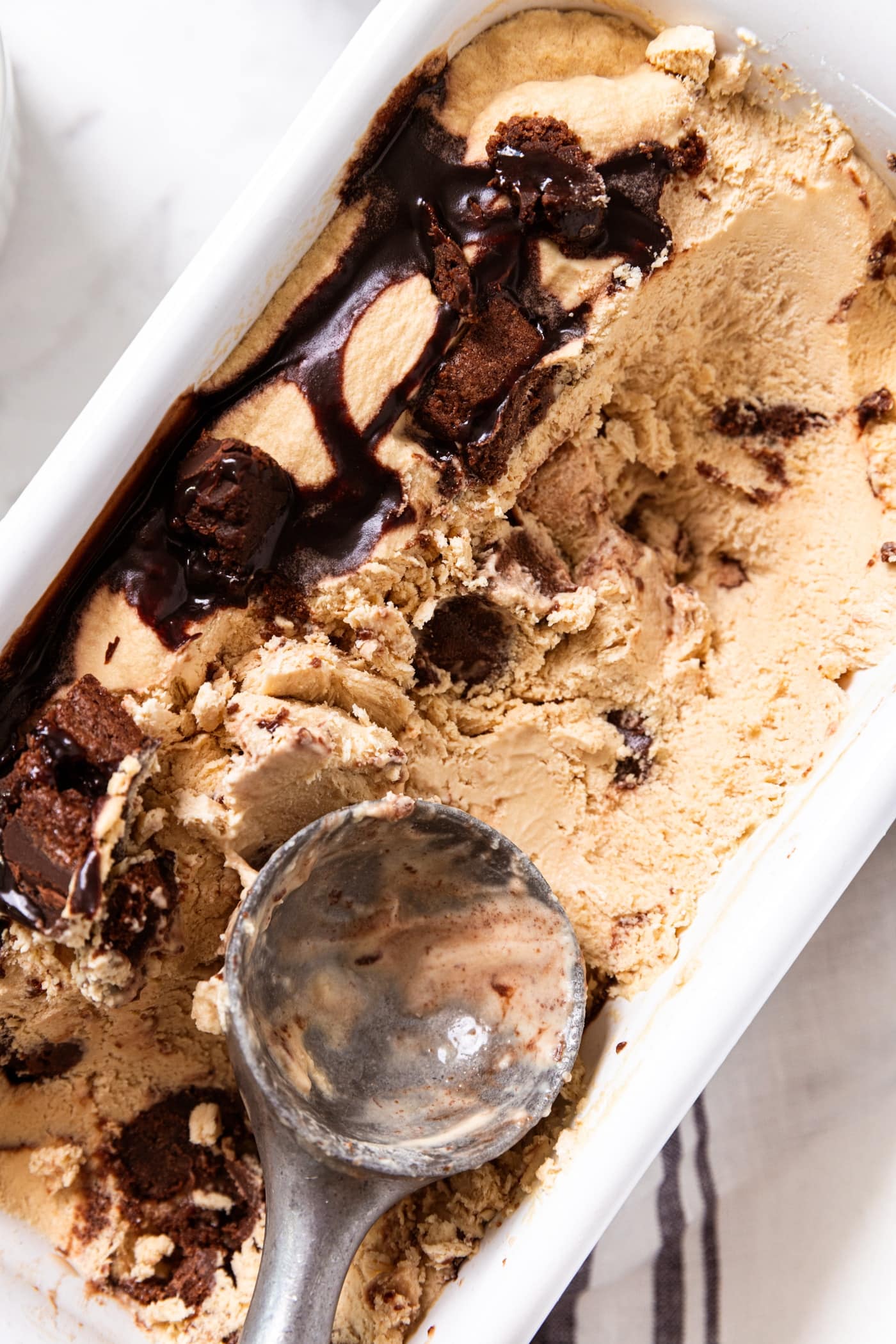 Ice cream scoop resting on espresso brownie no-churn ice cream in white loaf pan.