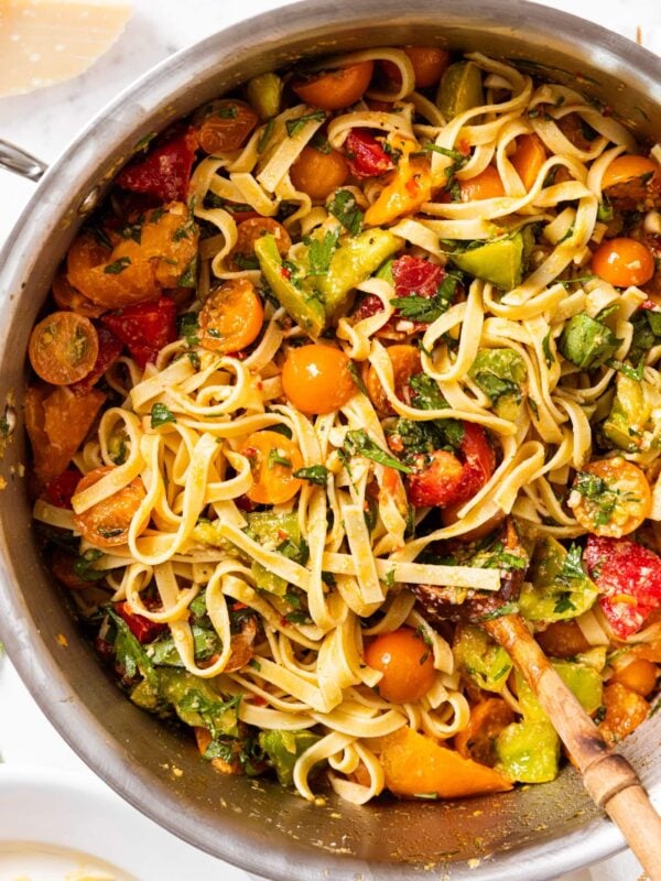 Metal pot filled with pasta mixed with tomatoes and fresh chopped herbs sitting on marble countertop.