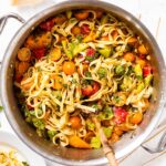 Large metal stockpot filled with pasta mixed with herbs and tomatoes all on marble surface.