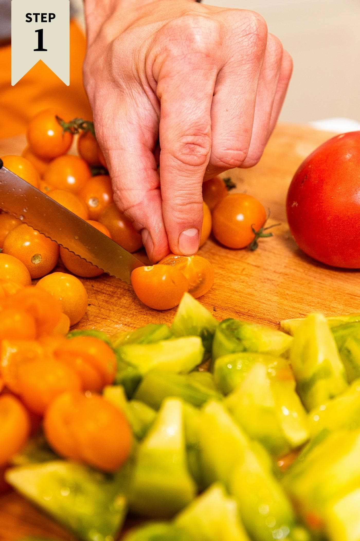 Hand slicing orange colored cherry tomato in half on cutting board with green tomatoes in front.