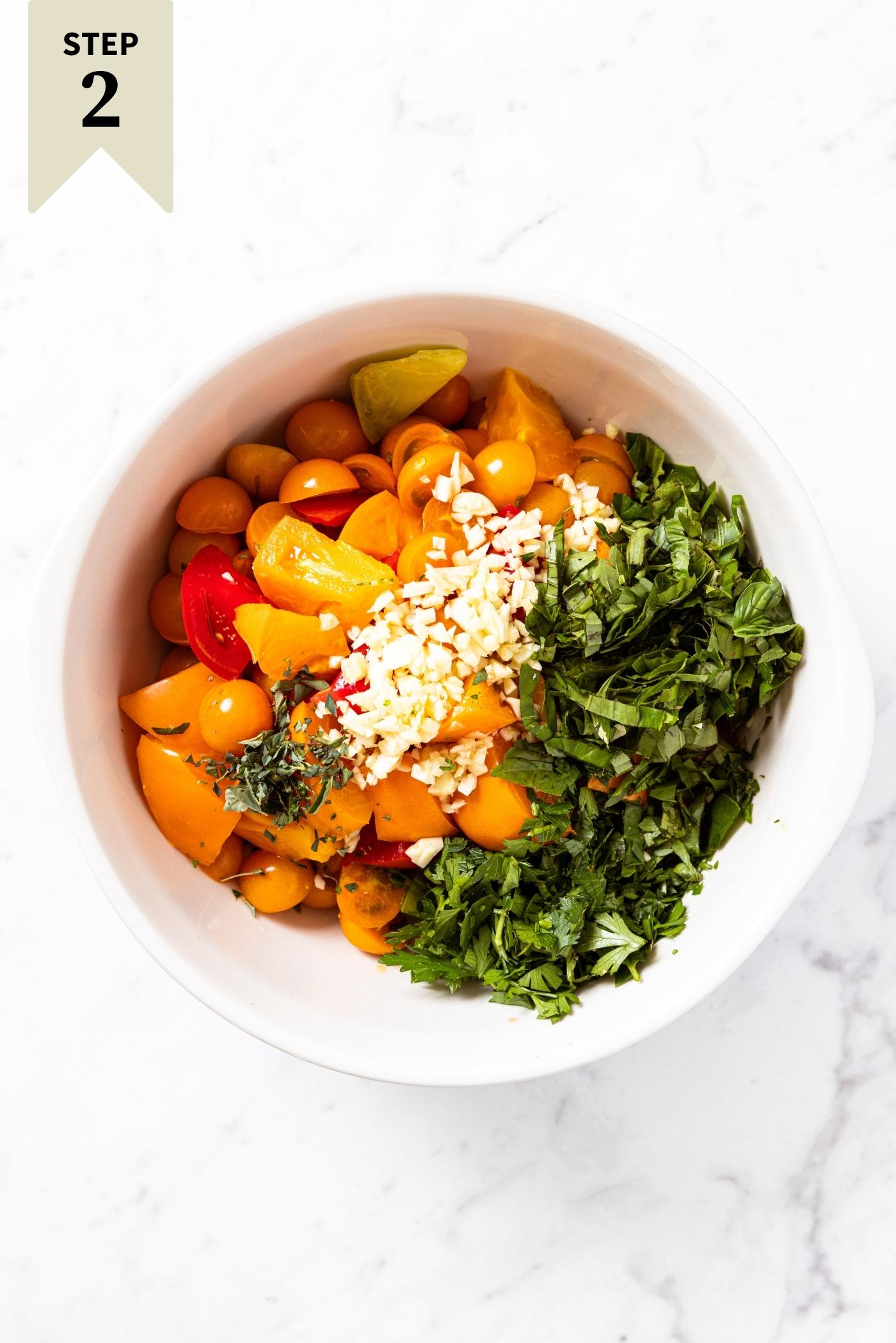 Multiple colors of tomatoes sitting in white bowl along with chopped fresh herbs and garlic on top.
