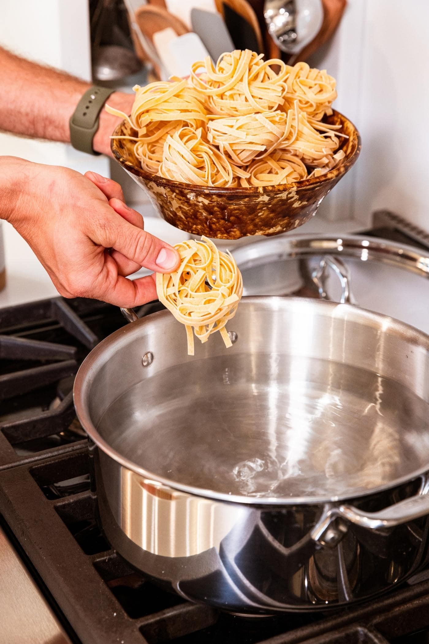 Hand placing pasta into large stockpot on stovetop filled with water.
