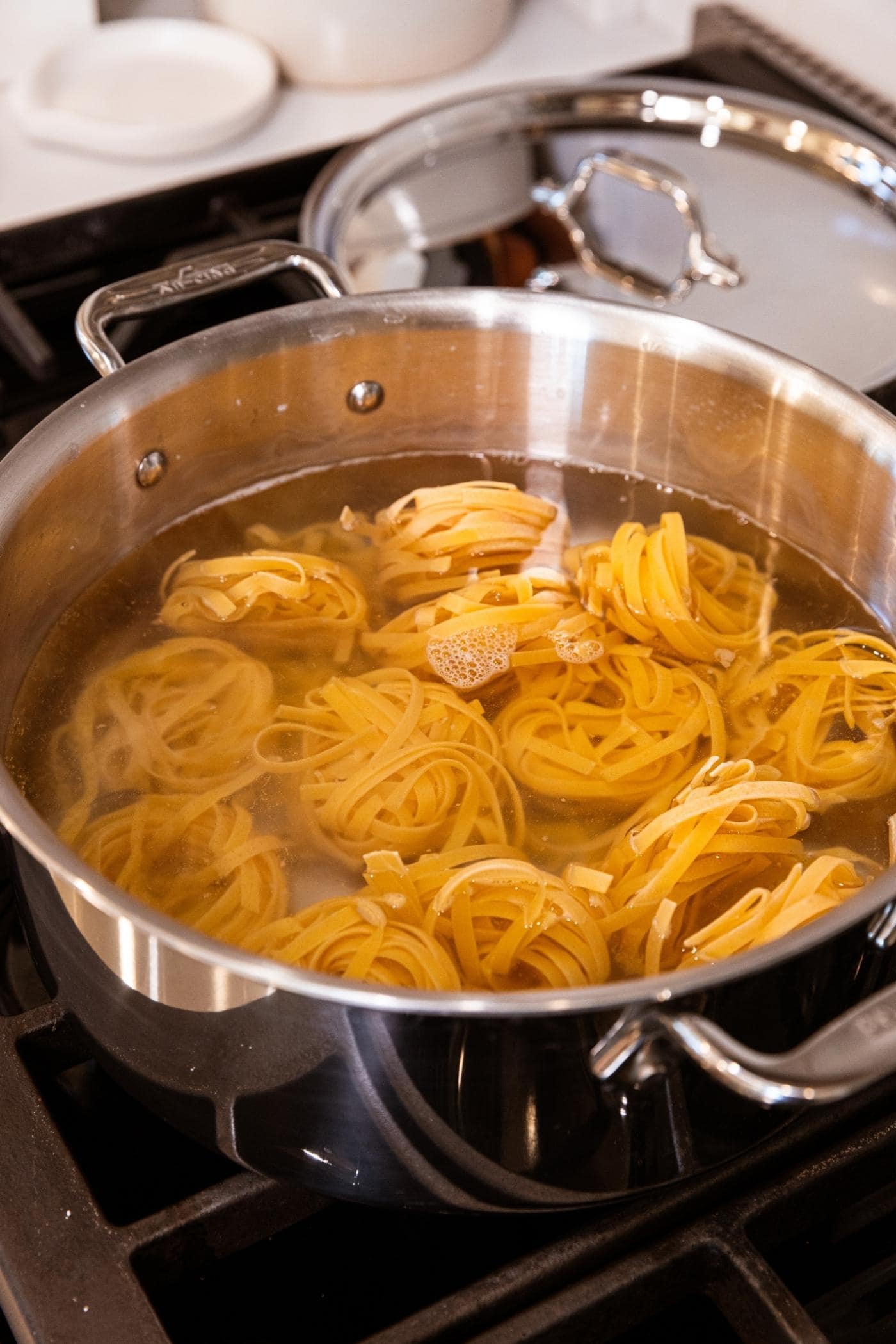 Large stockpot on stovetop filled with water and pasta wrapped into round nests.