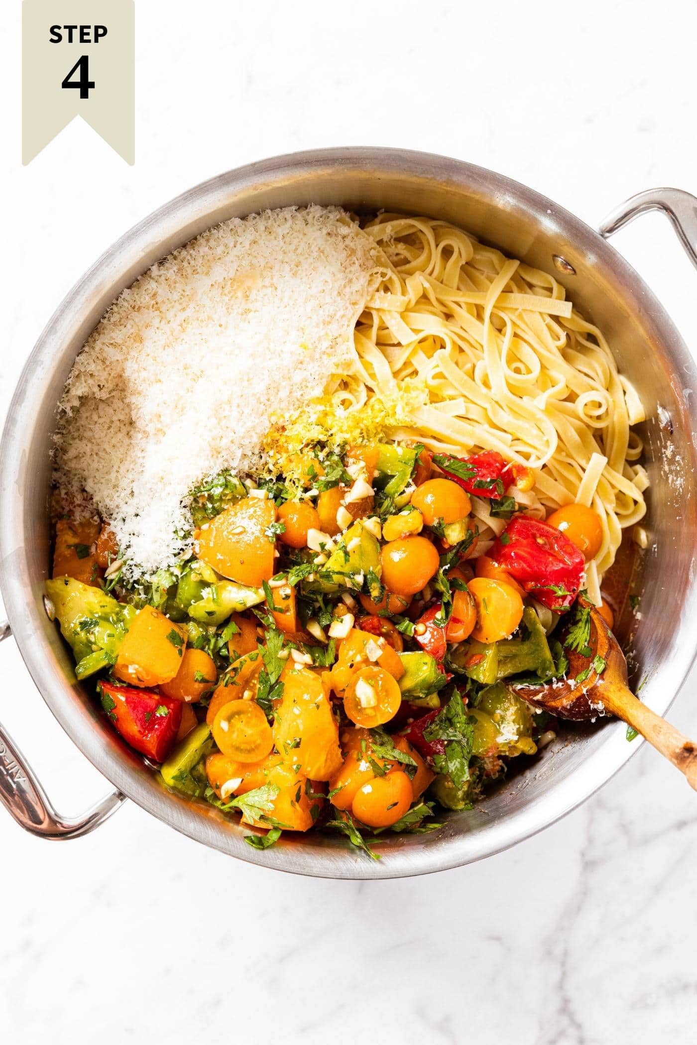 Large metal stockpot sitting on marble countertop with pasta, tomatoes, herbs, and Parmesan cheese, all unmixed with each other.