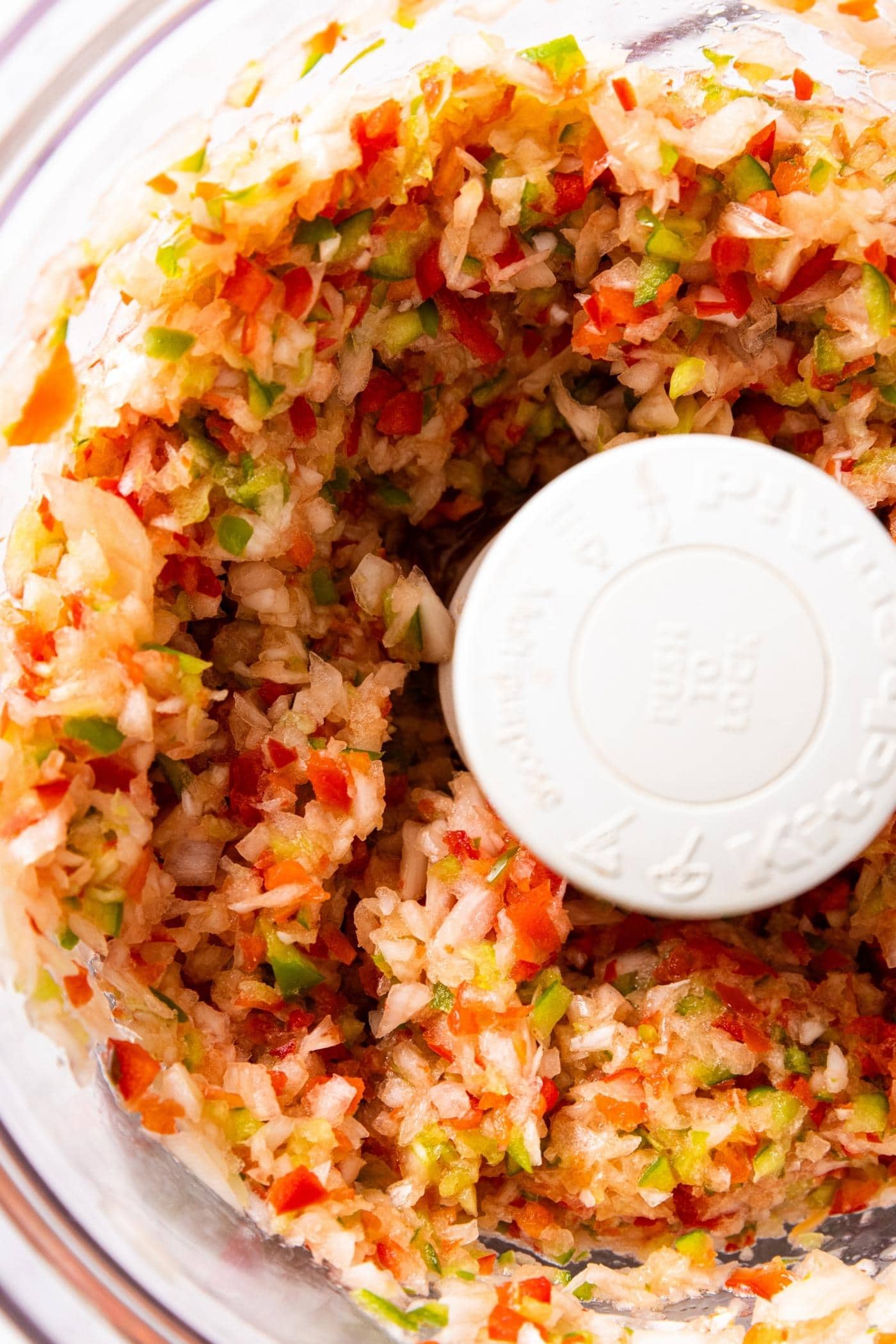 Chopped up red and green bell pepper and onion sitting in food processor bowl.