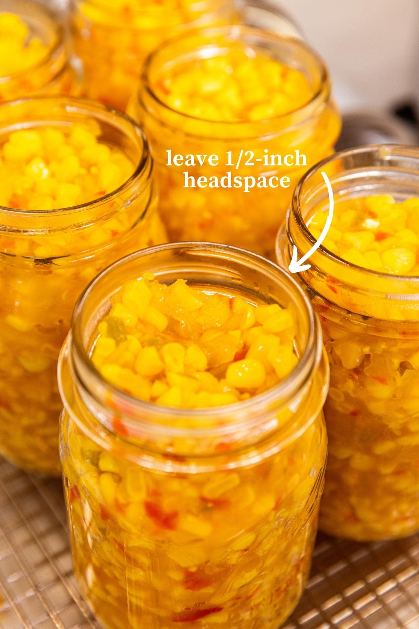 Glass jars filled with corn relish in glass jars after cooking on the stove with words on picture indicating the space at the top of the jar.