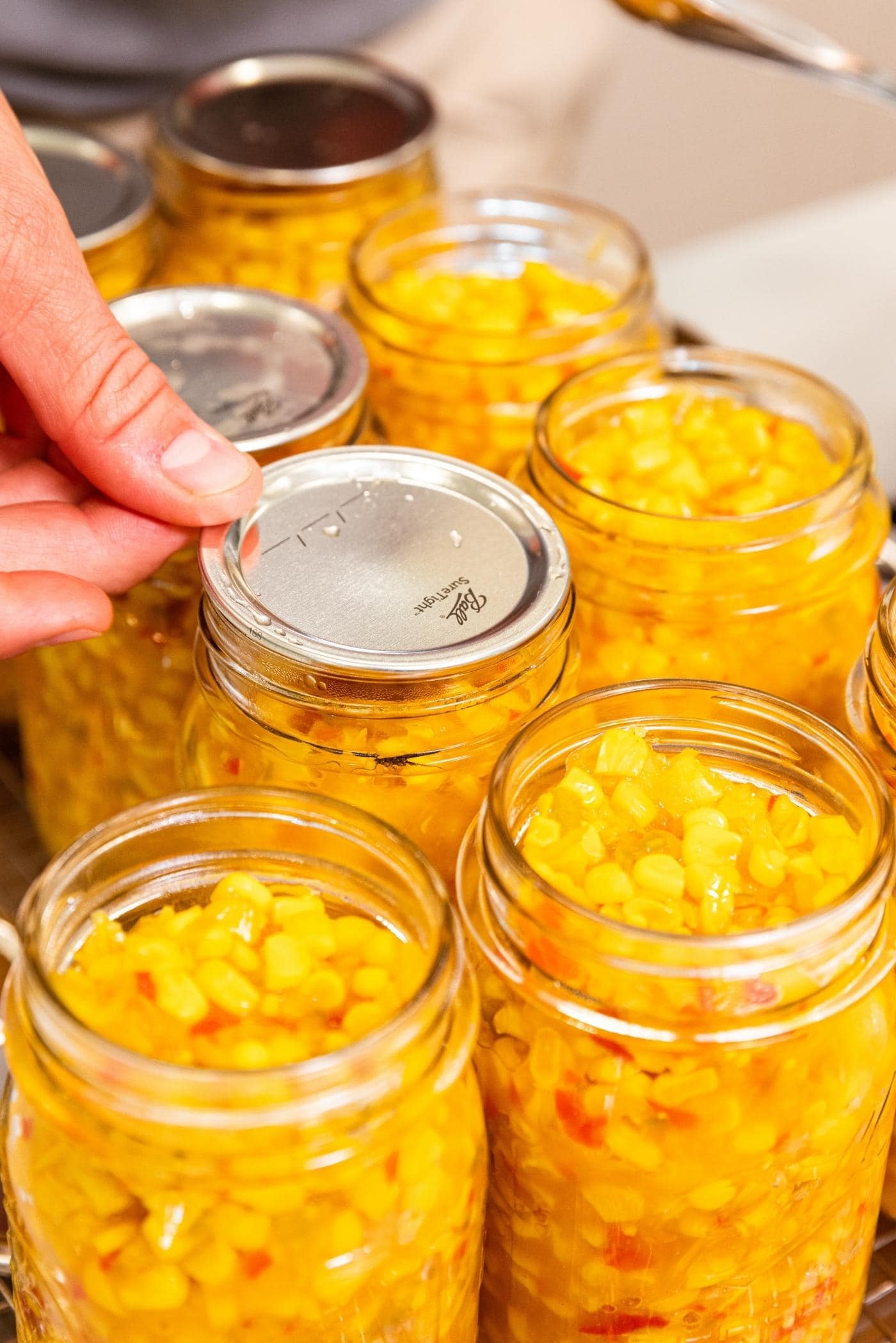 Hand placing lid on top of glass jar filled with corn relish.