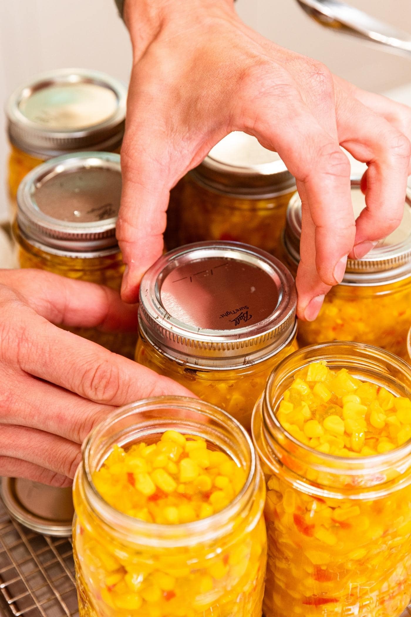 Hand affixing lid and ring to top of glass jar filled with corn relish.