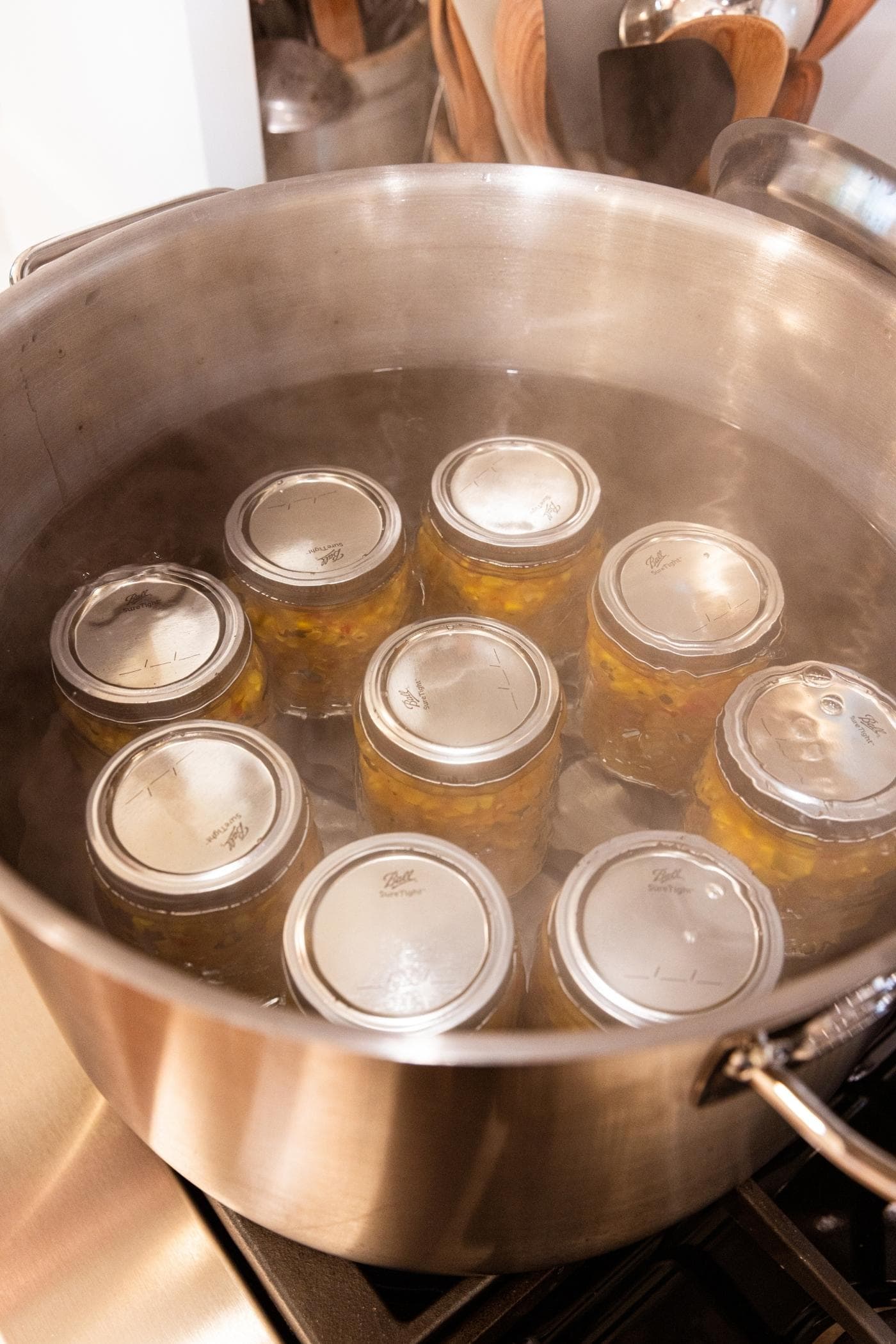 Metal stockpot filled with nine glass jars with water covering the top sitting on stovetop ready to be water bathed.