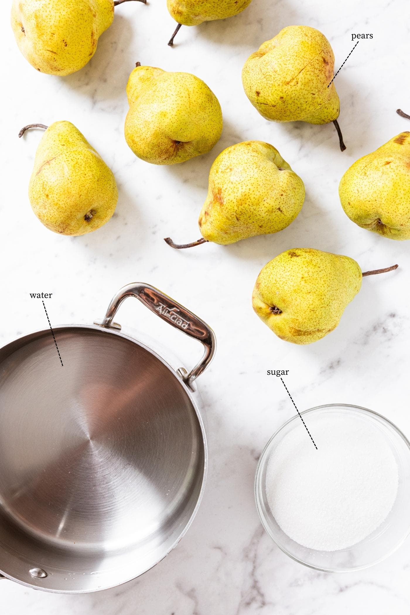 Marble surface filled with the ingredients needed to can pears including ripe pears, water in a kettle, and sugar in a glass bowl.