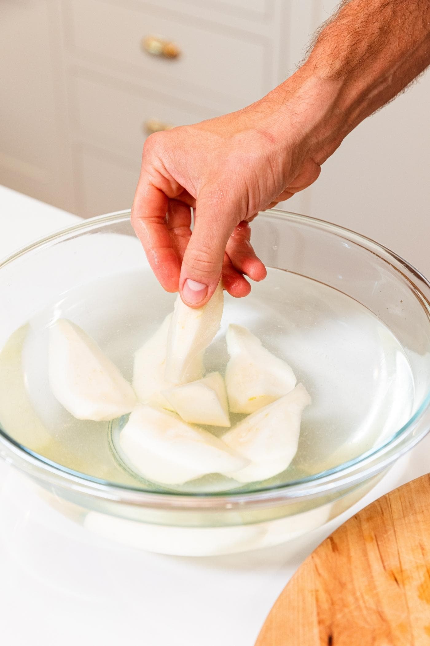 Hand placing slice of pear into a bowl filled with water and additional pears to keep them from browning.