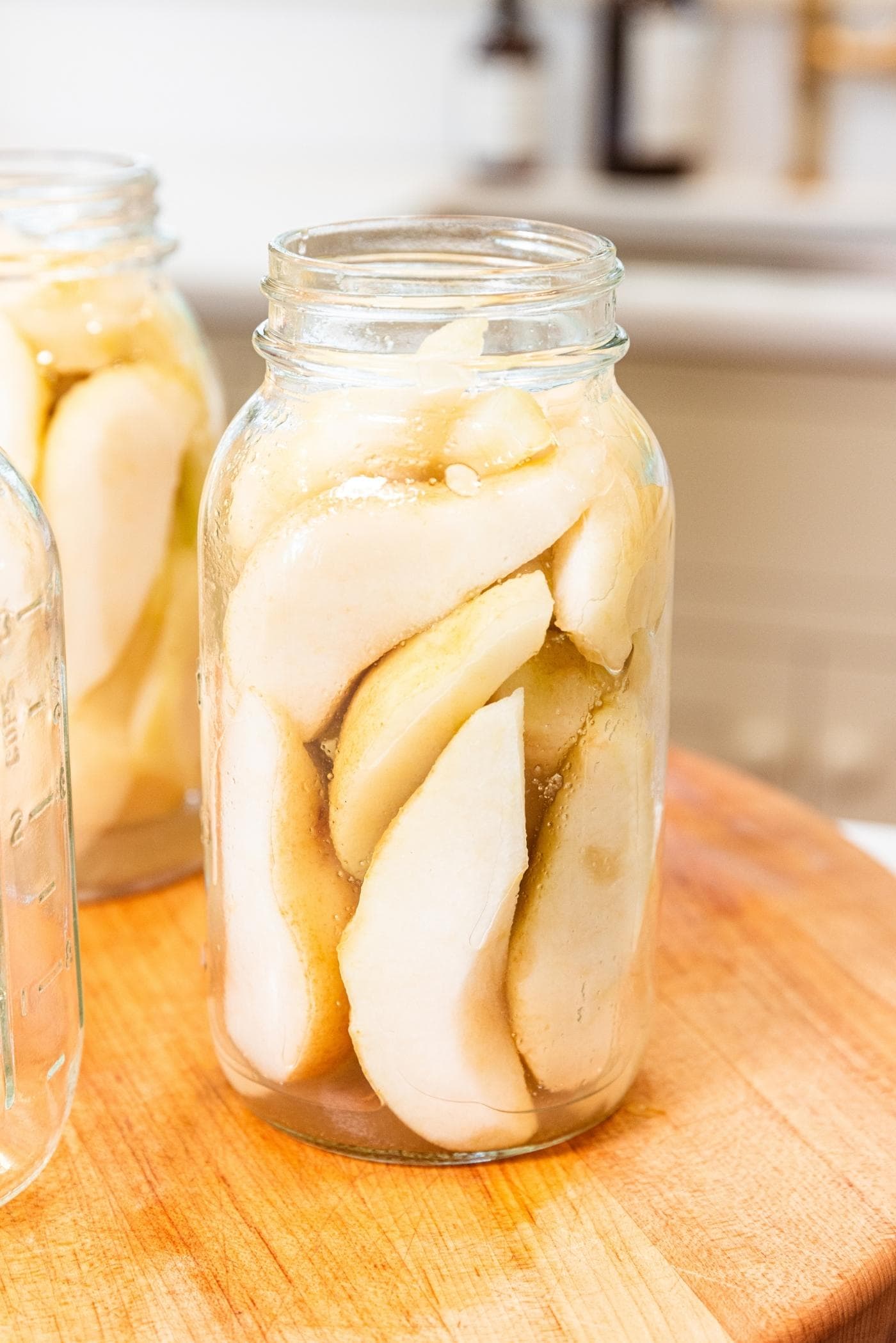 Glass canning jar sitting on wooden cutting board filled with slices of pears with more jars in background.
