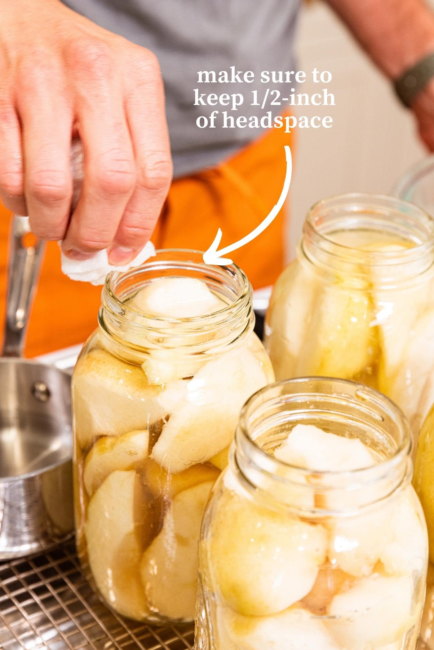 Hand wiping off the rim of a glass canning jar filled with slices of pears and sugar syrup.