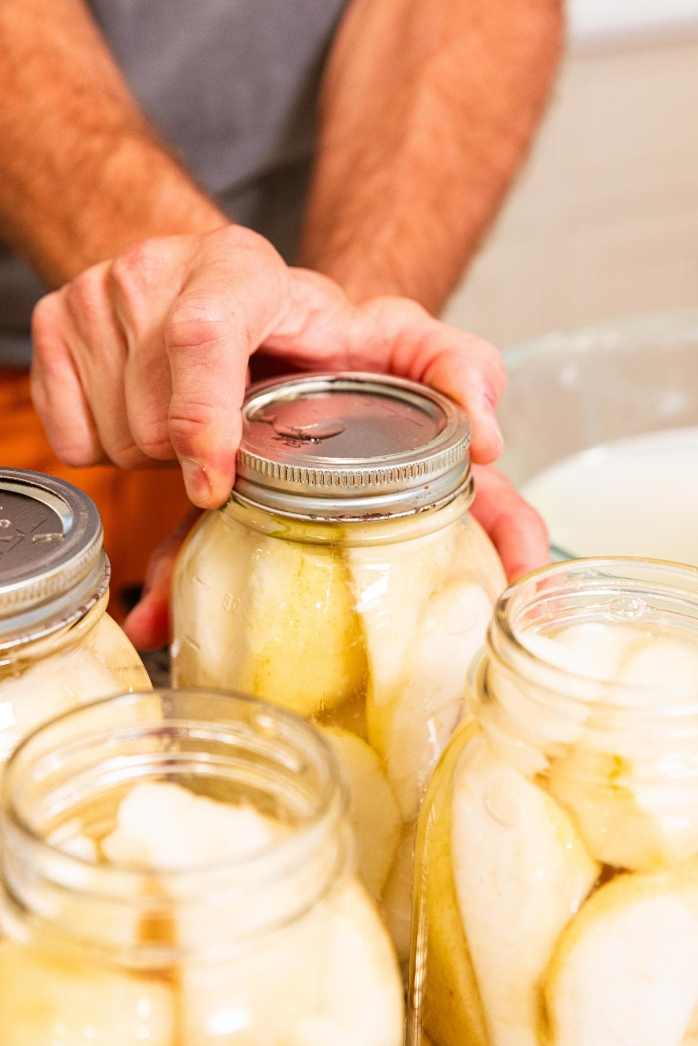 Hand screwing lid of canning jar filled with slices of pear.