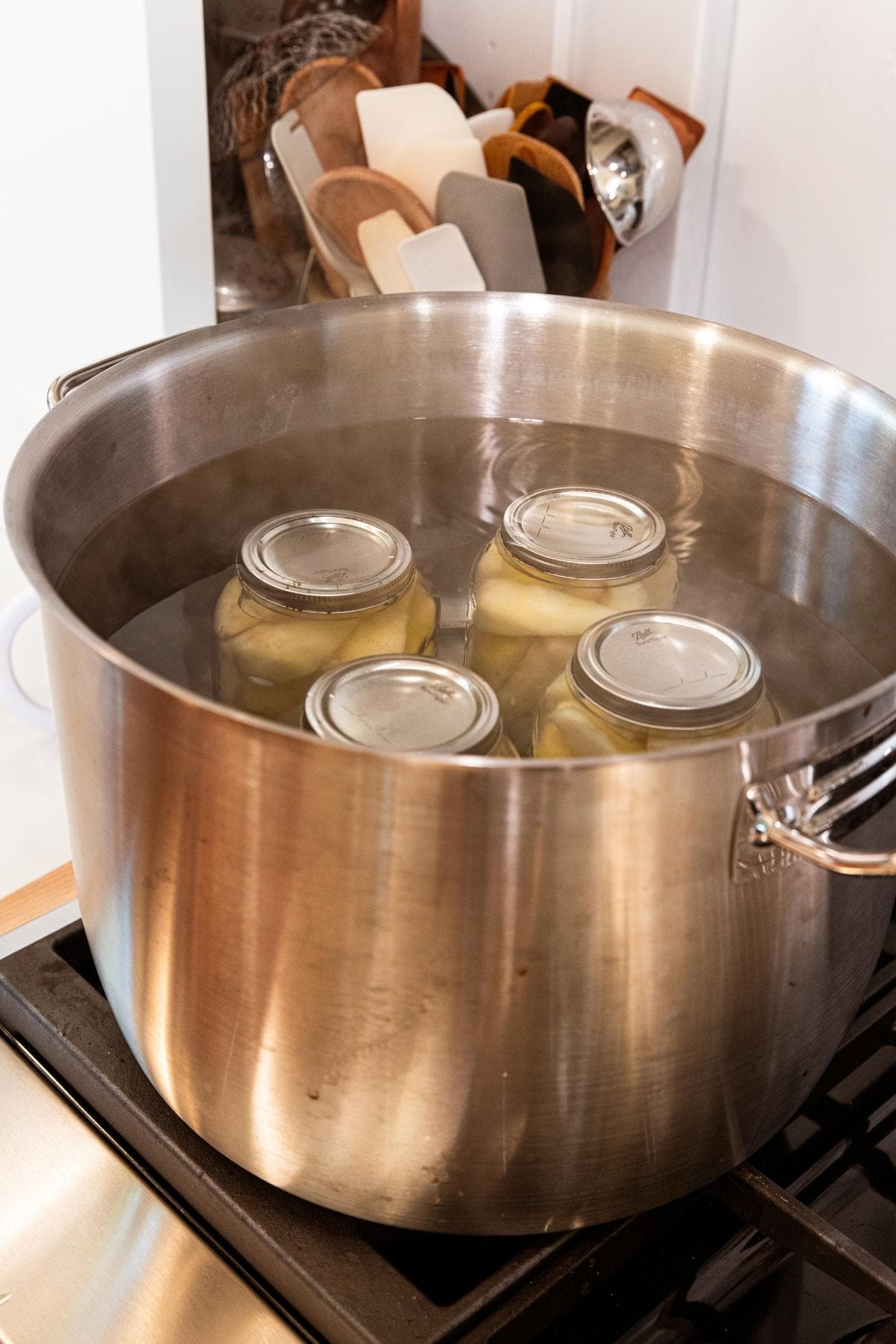 Large canning pot filled with jars of pears with lids and rings on top with water covering entire surface of jars all on stovetop.