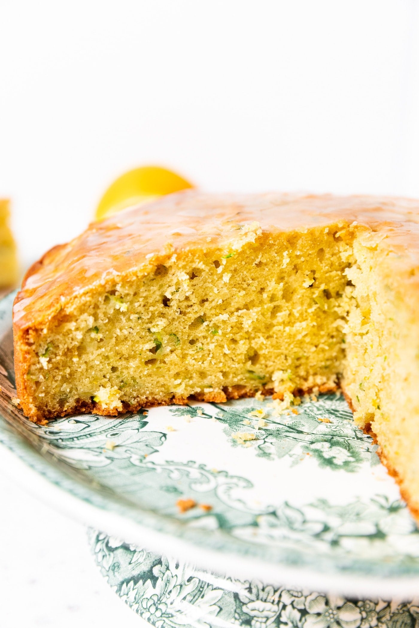 Olive oil cake with slices missing sitting on green cake plate showing the interior texture of the cake with white background.