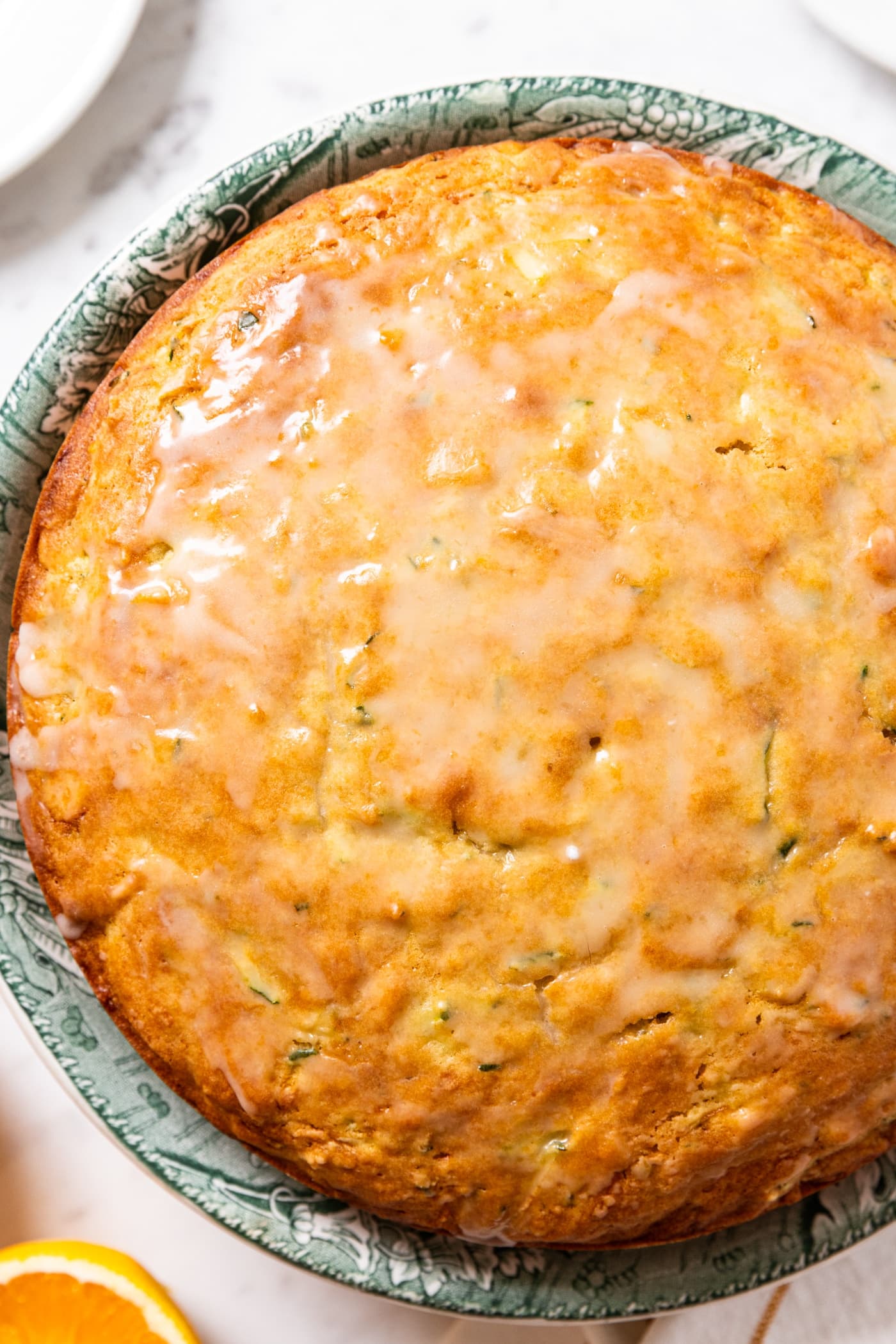Olive oil cake topped with almost clear glaze sitting on green colored cake plate on white countertop.