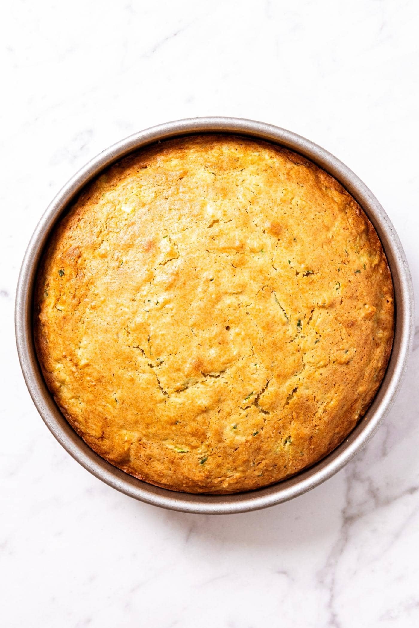 Baked cake fresh from the oven still in the baking pan with golden crusty top sitting on marble surface.