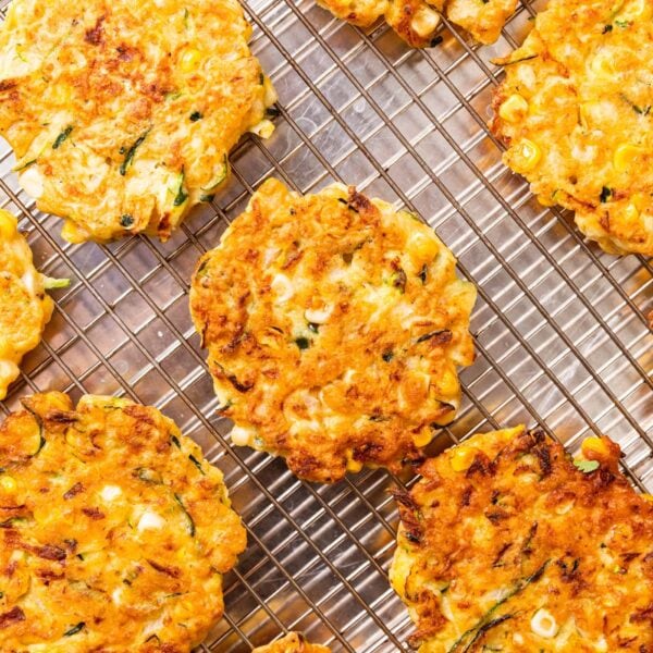 Round browned zucchini and corn fritters sitting on wire cooling rack after coming out of the cooker with browned edges.