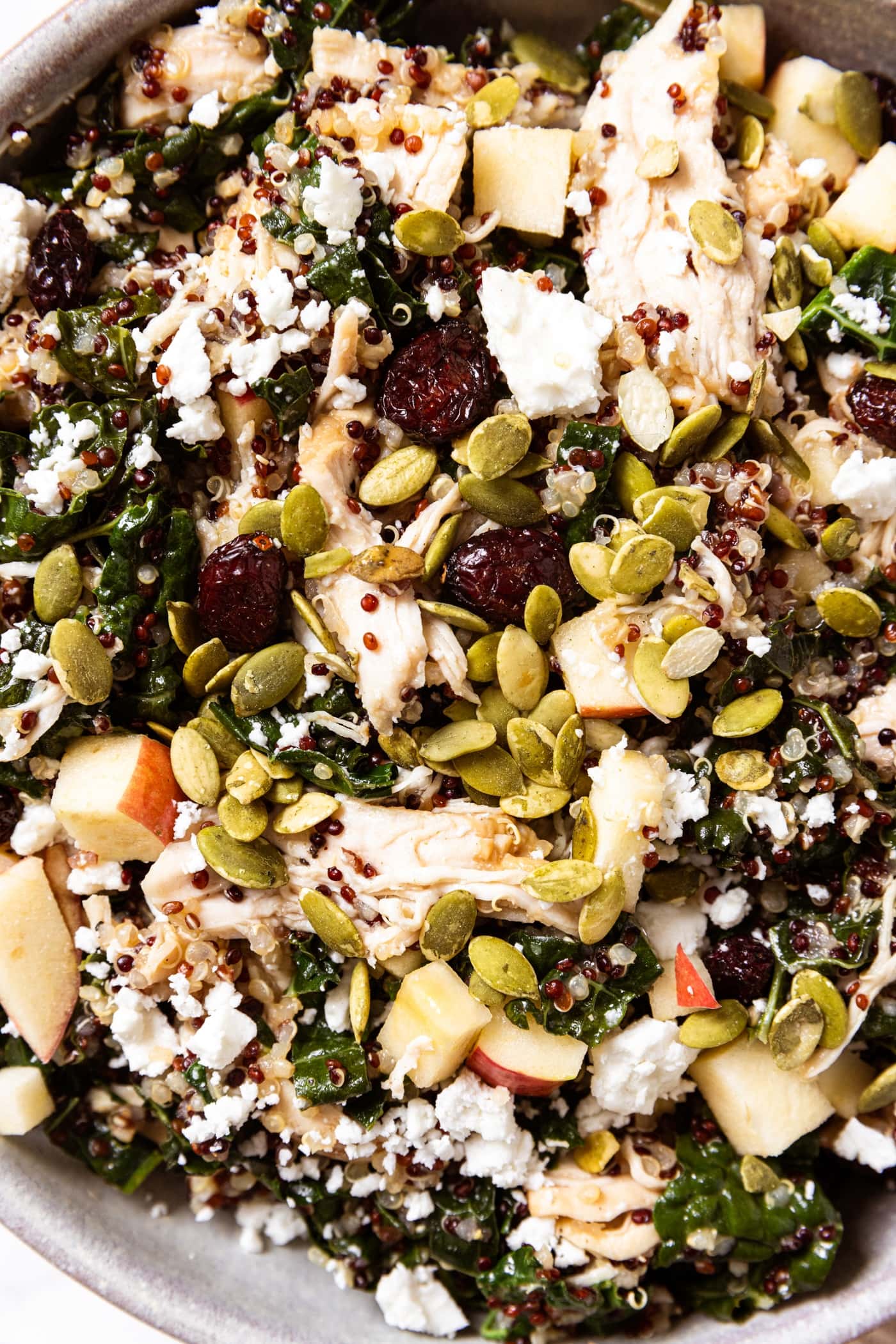 Stoneware bowl filled with quinoa kale salad topped with pumpkin seeds, chopped apple, shredded chicken, and more.