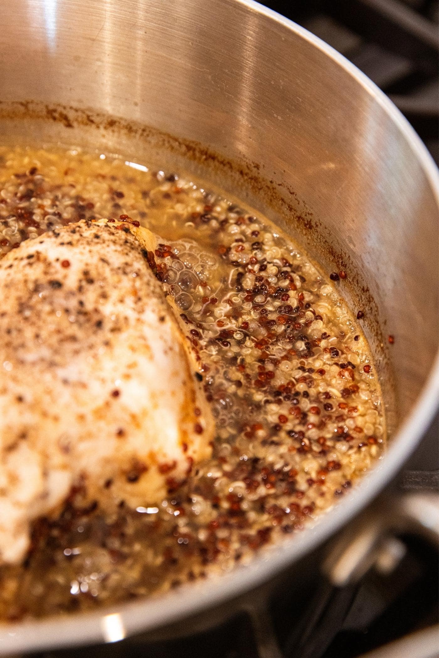 Quinoa simmering in apple cider liquid in kettle on stove along with poached chicken breast.