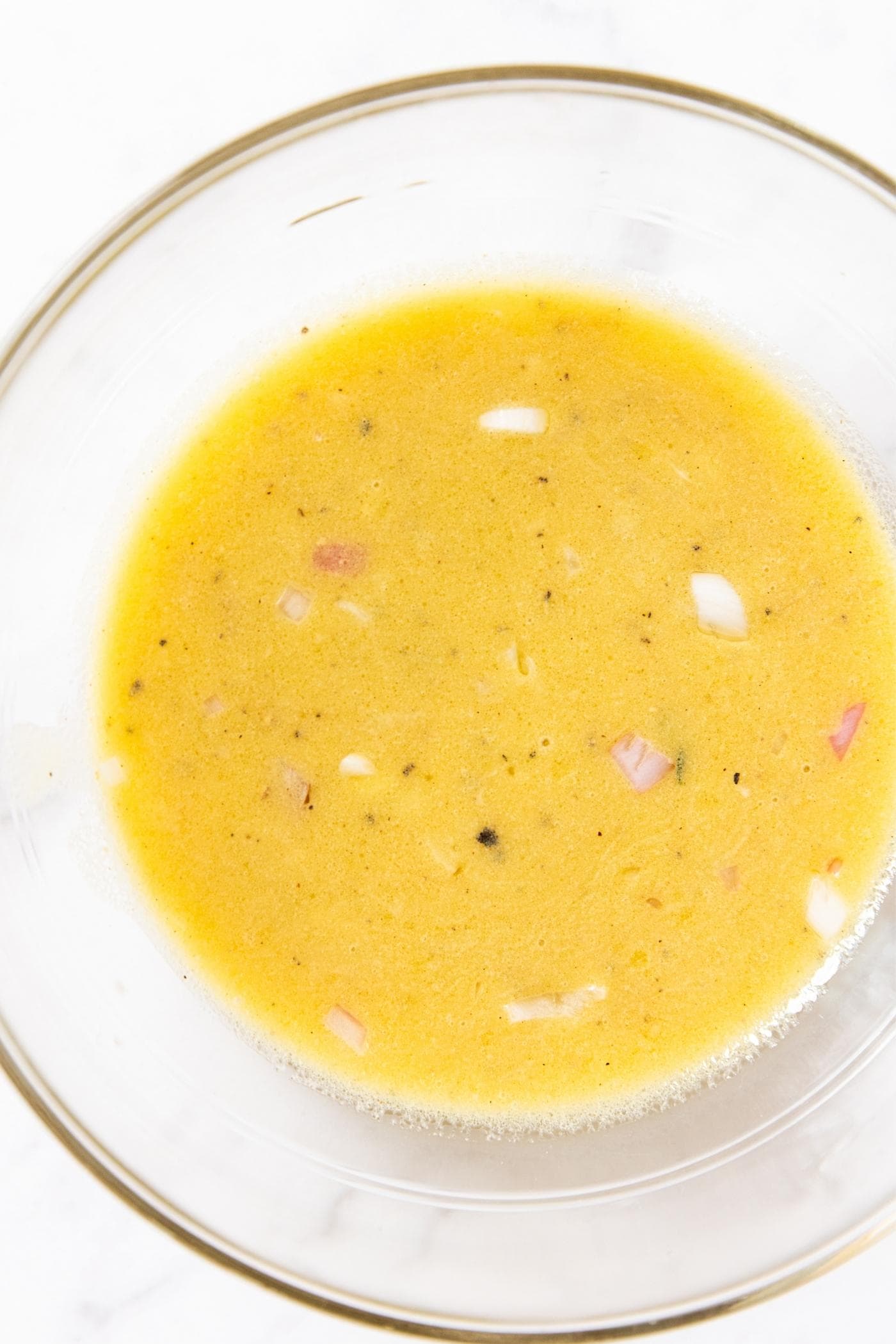 Glass bowl sitting on white surface filled with yellow colored salad dressing.
