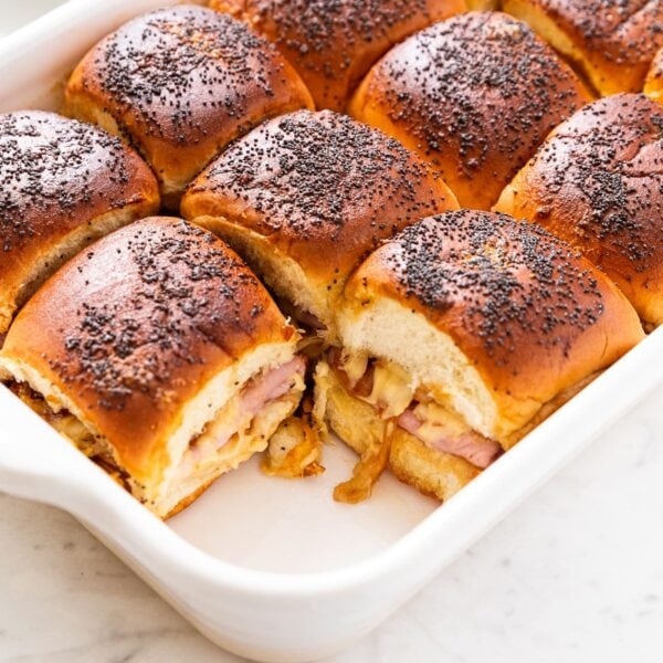 White baking dish sitting on marble surface with baked ham and cheese slider sandwiches inside after coming out of the oven.