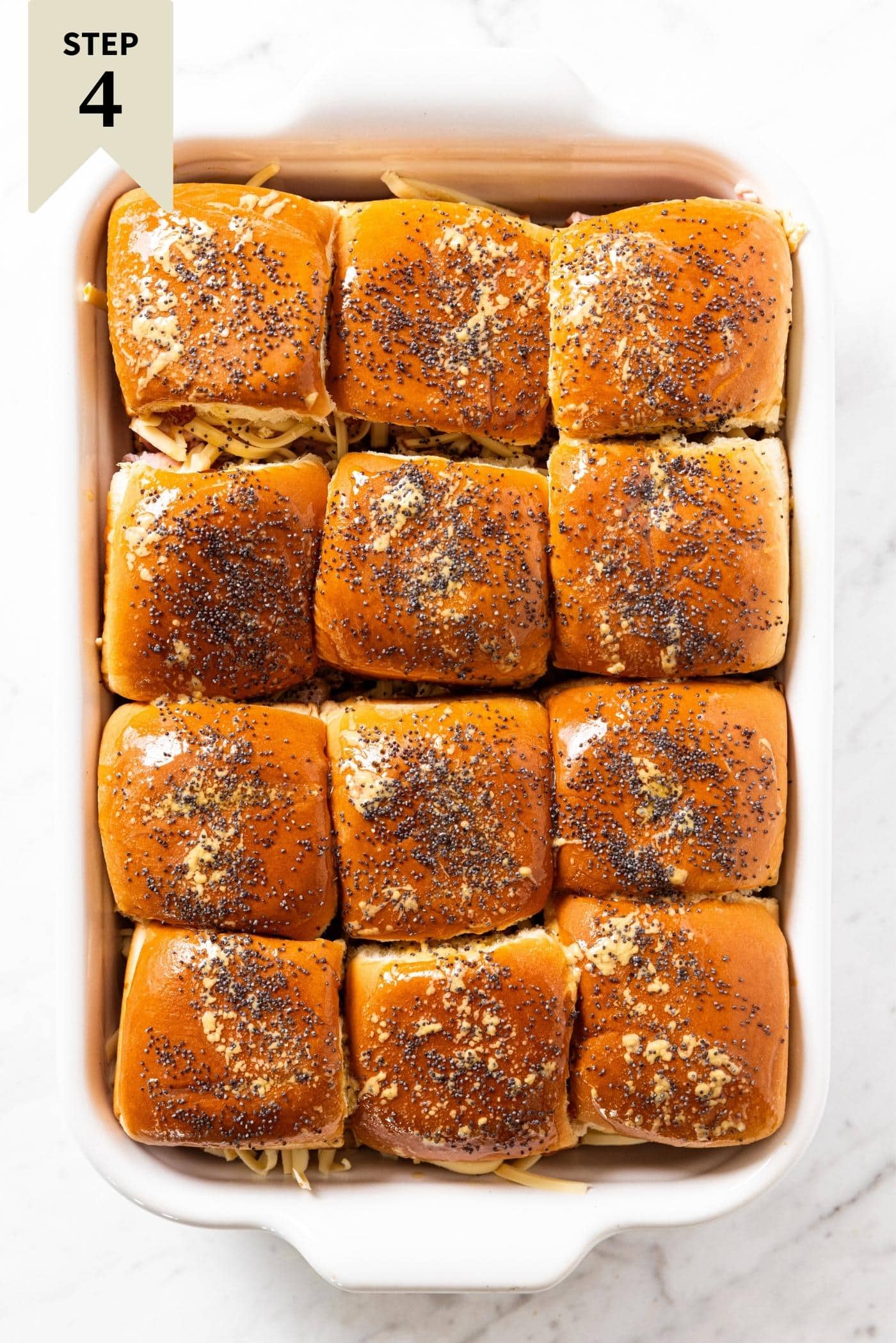 White baking dish filled with sandwich buns sprinkled with poppy seeds before going into the oven for a final baking.