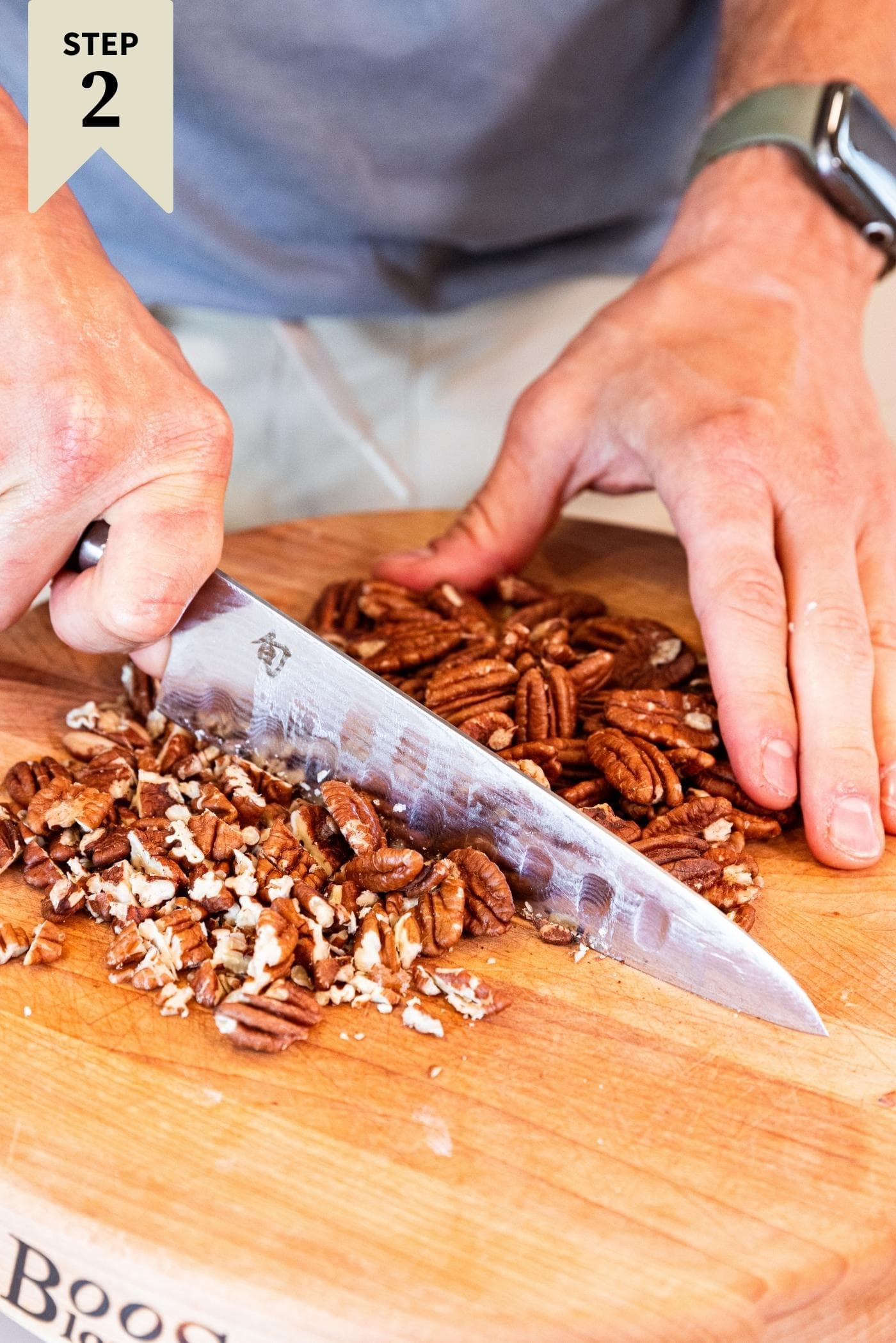 Hand chopping pecans on wood cutting board.