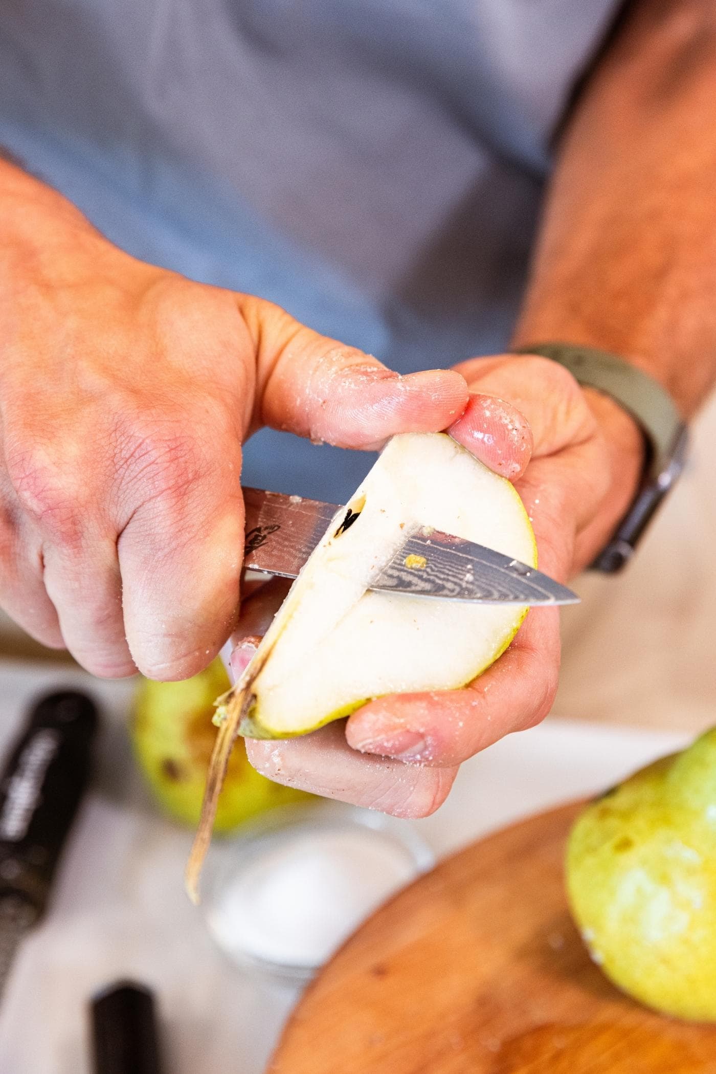 Hand slicing out the center core of an unpeeled pear with more pears in background.