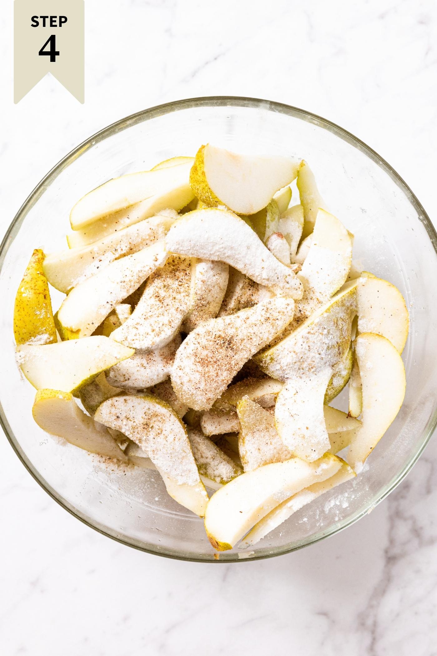 Slices of pears sitting in glass mixing bowl with sugar and spices sprinkled all over the top.