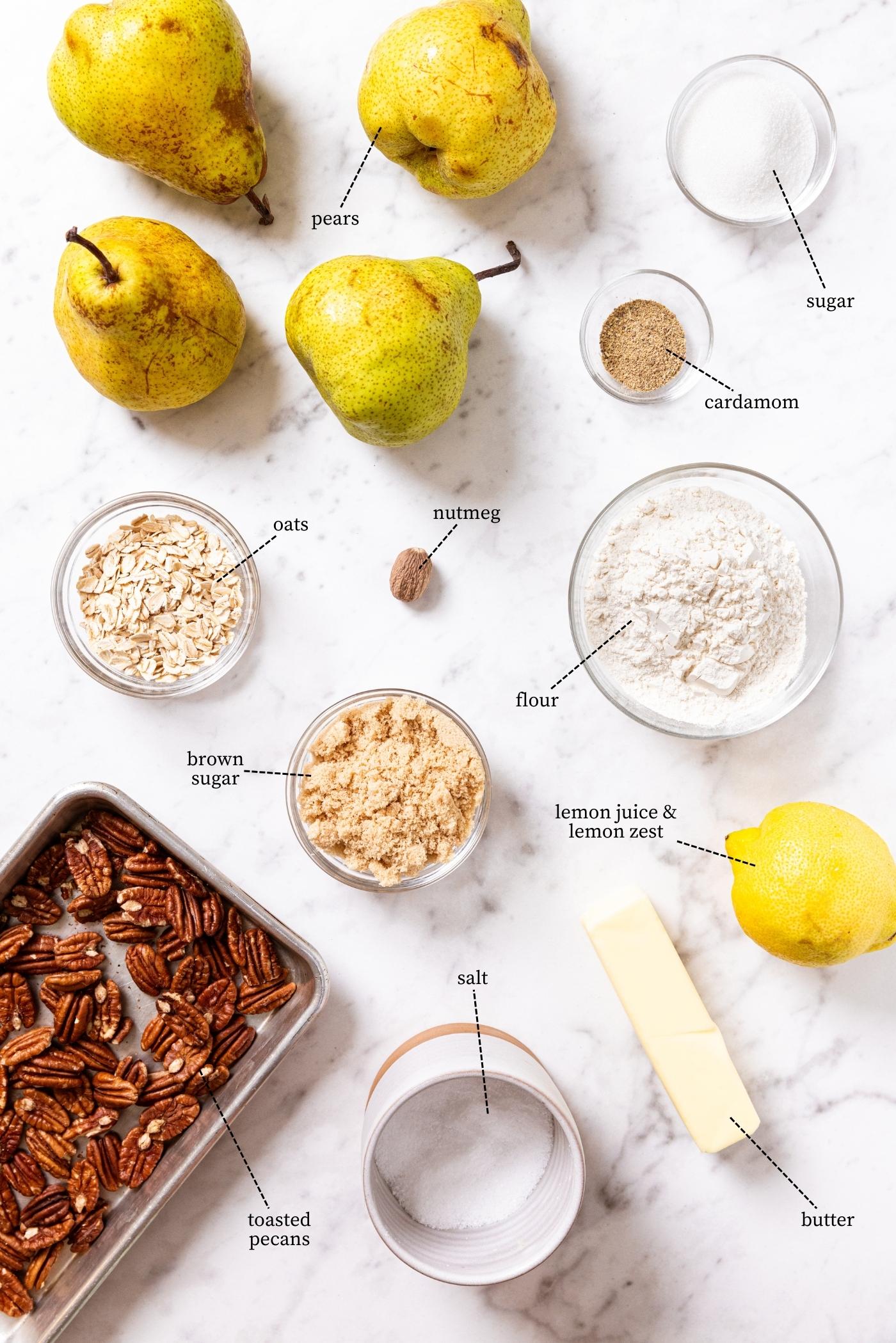 White marble surface filled with all the ingredients needed to make skillet pear crisp including pears, sugar, flour, lemon, nuts, and more.